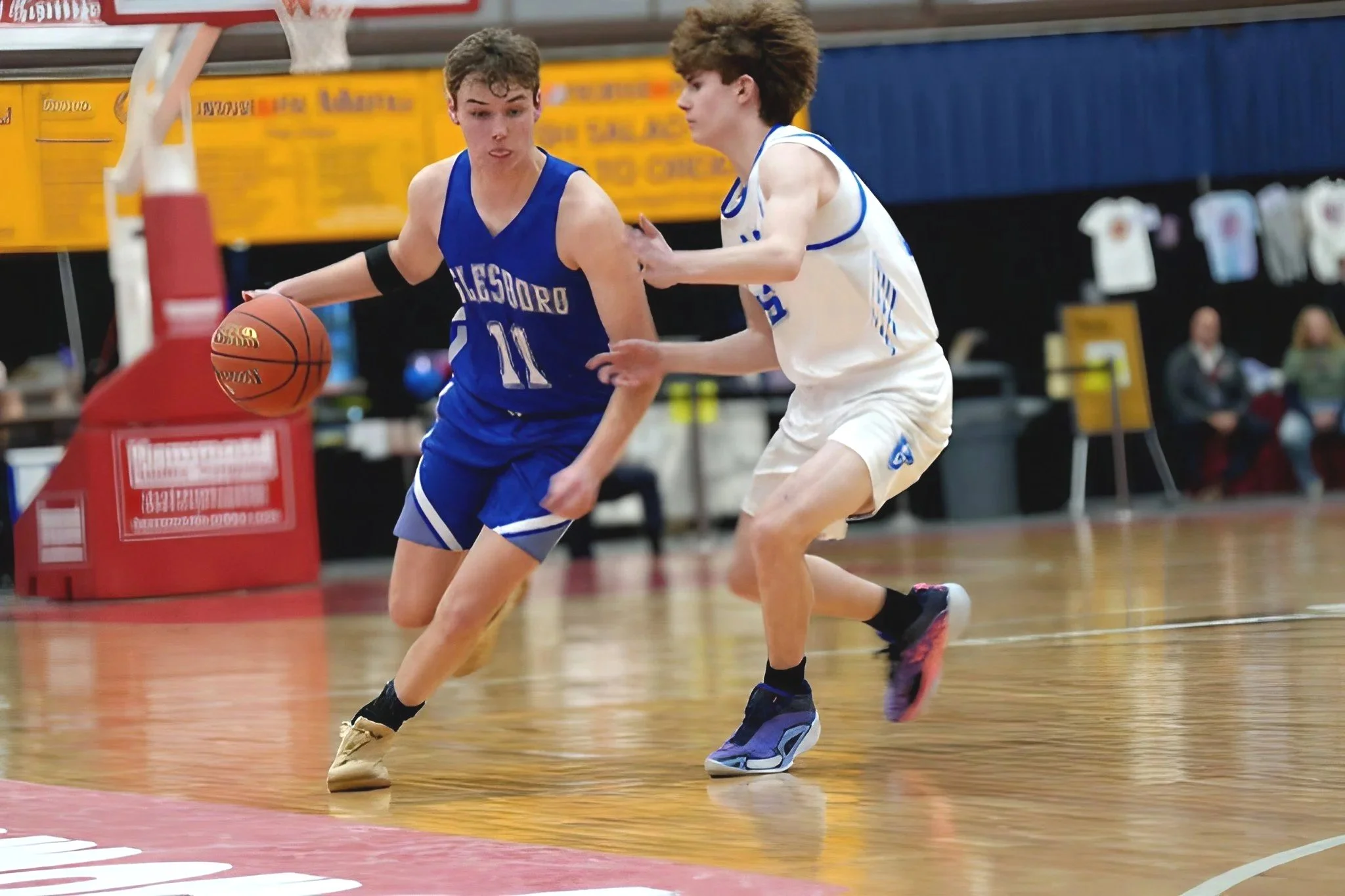Two young male basketball players competing for the ball during a game on an indoor court.