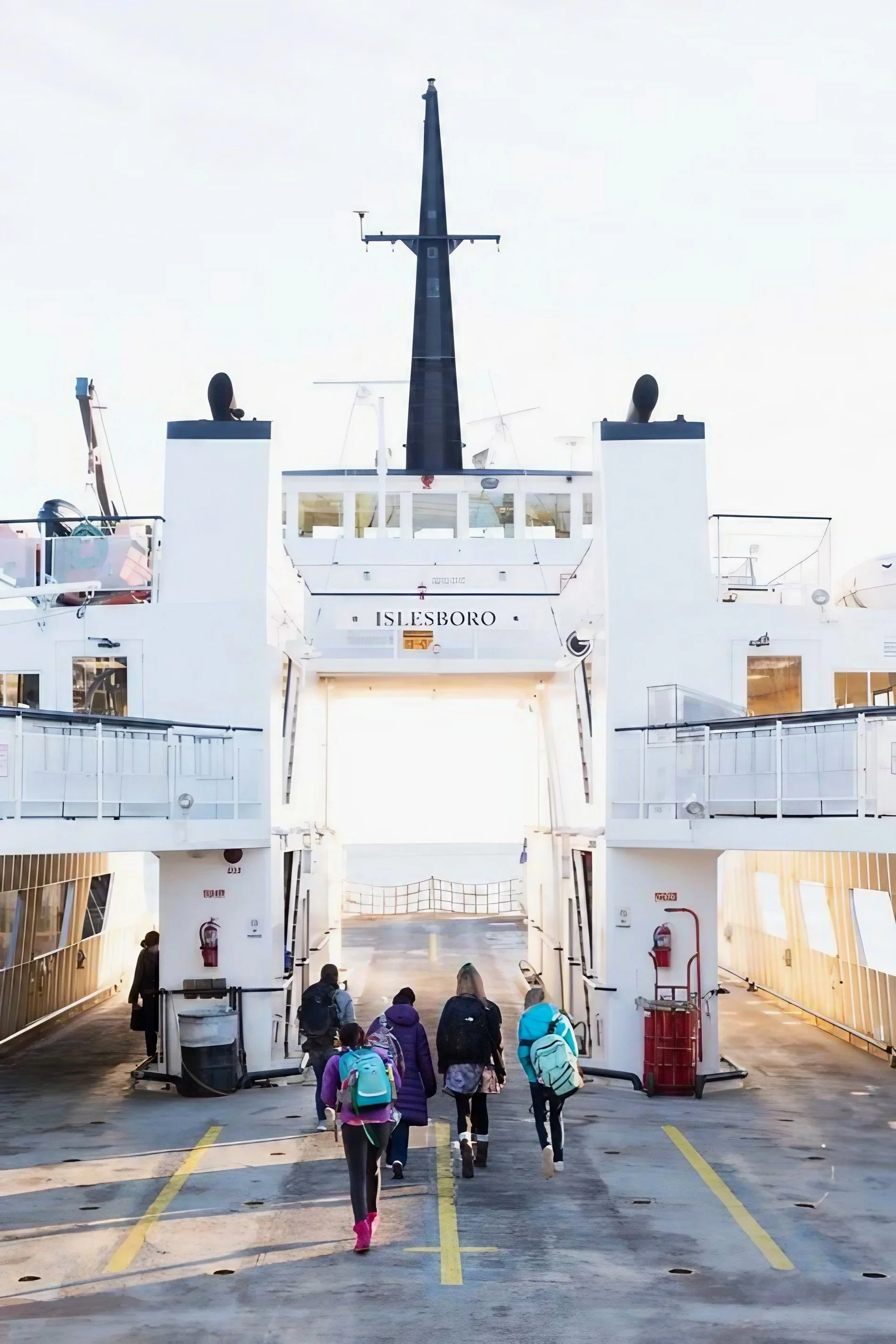 People boarding a cruise ship named 'Islesboro' at a port. The ship's gangway is lowered, and passengers with backpacks are walking up the ramp to board.
