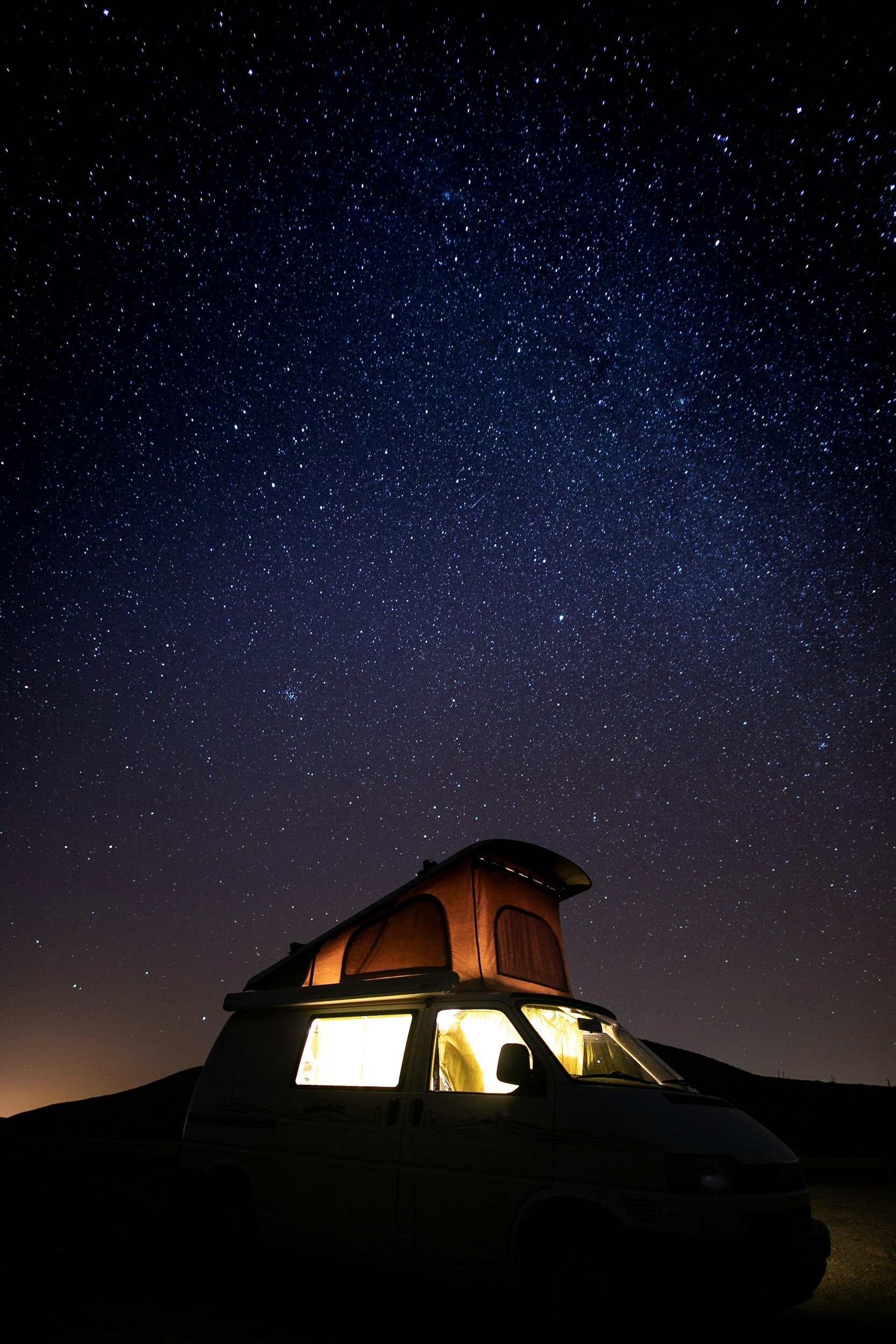 The photo features a campervan with a pop-up roof at night, parked outdoors, with a star-filled sky overhead.