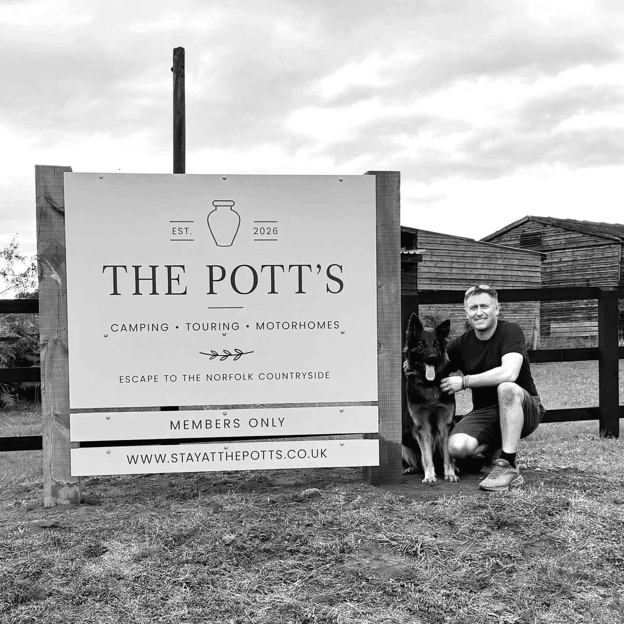 Black and white photo of a man sitting on the ground with a dog, standing next to a sign that reads "The Pott's," with smaller text below about camping, touring, and motorhomes, and a website URL.
