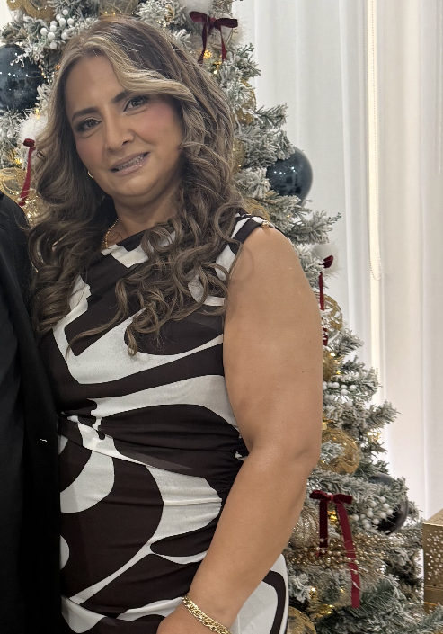 Woman with curly hair wearing a black and white sleeveless dress, standing in front of a decorated Christmas tree.