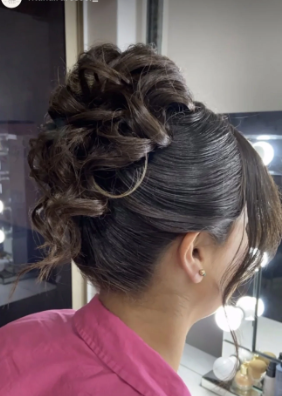 Upside-down view of a woman with dark hair styled in an elegant updo, wearing a pink top, in a salon setting.