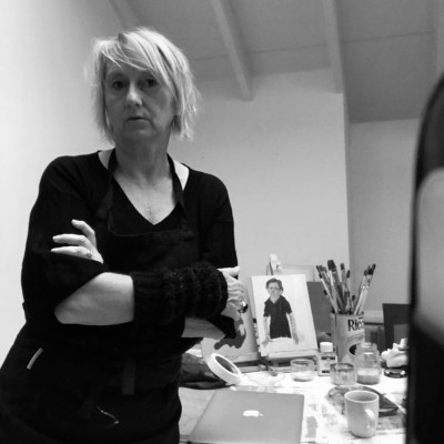 Vrouw met kort, warrig haar staat in een kamer met platen en kunstbenodigdheden op een tafel.