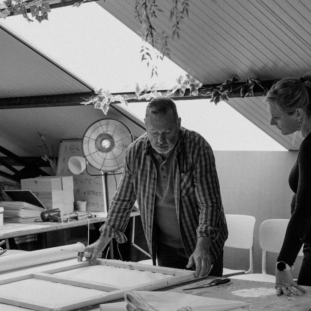 Twee mensen werken samen aan een kunstwerk of mogelijk een raam binnen een atelier.