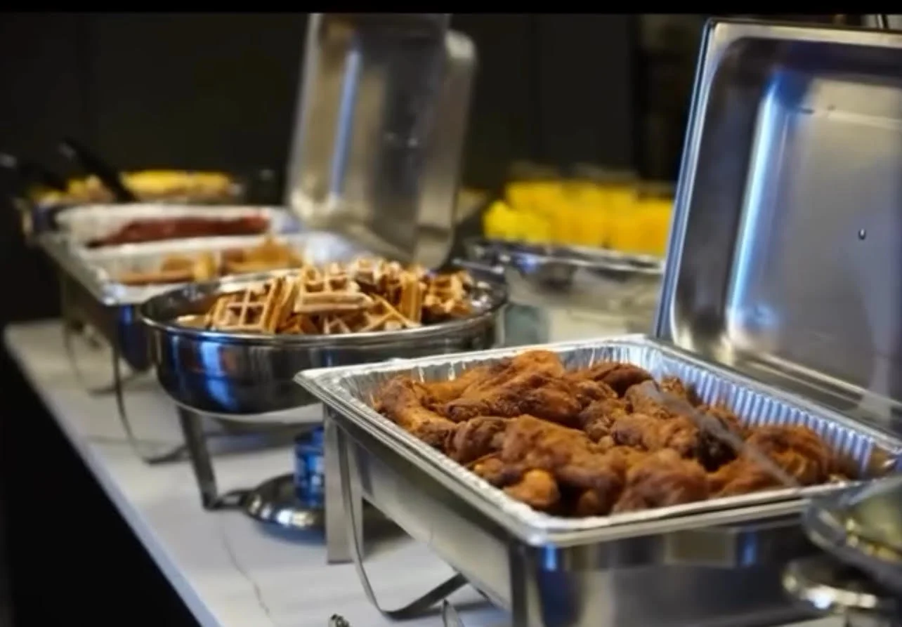 Buffet table with trays of fried chicken, waffle fries, waffles, and other breakfast foods