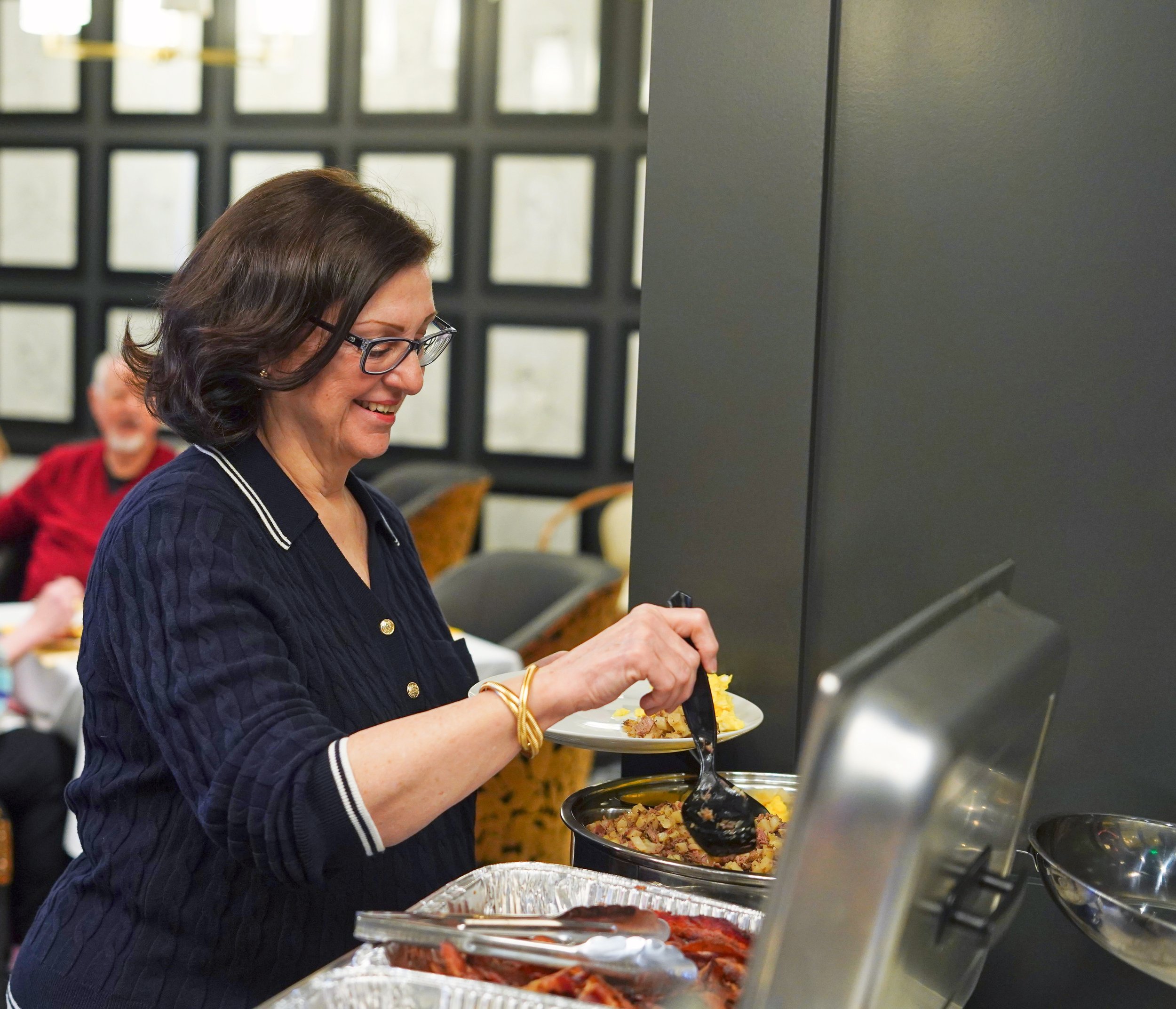 Woman serving herself food at a buffet with multiple trays of food.