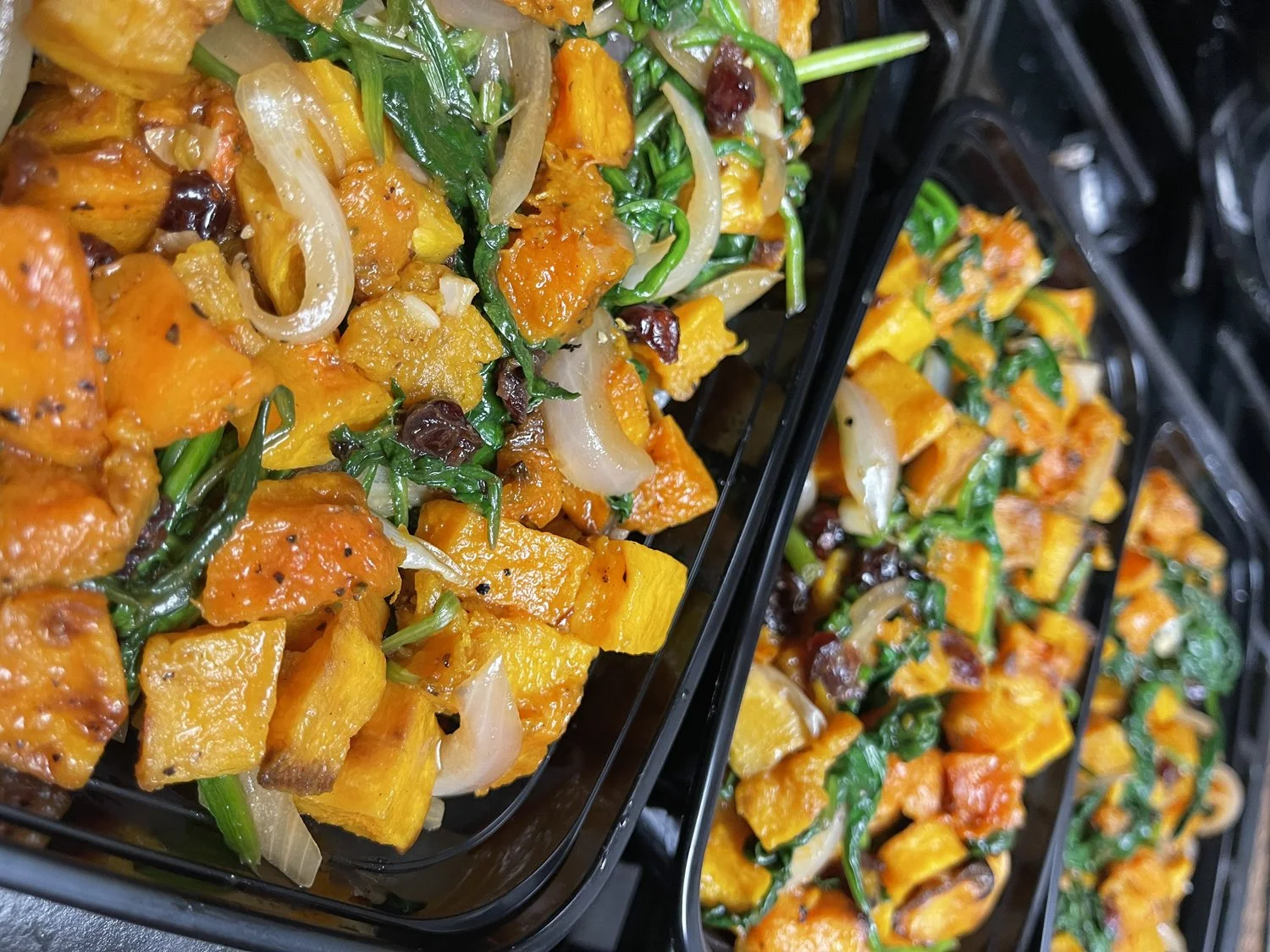 Close-up of cooked butternut squash, onions, spinach, and cranberries in a black tray.