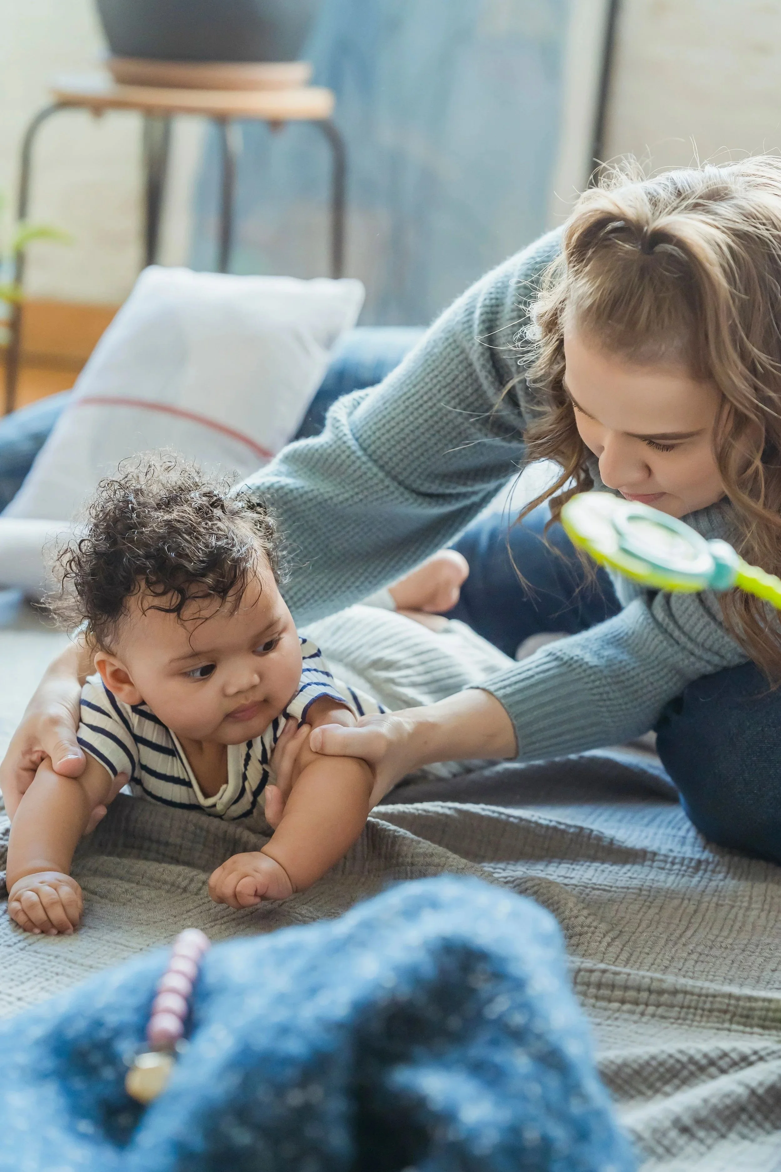A mother helping her pre-crawling baby achieve a better position on his tummy during an individual session of the Tummy Time! Method.