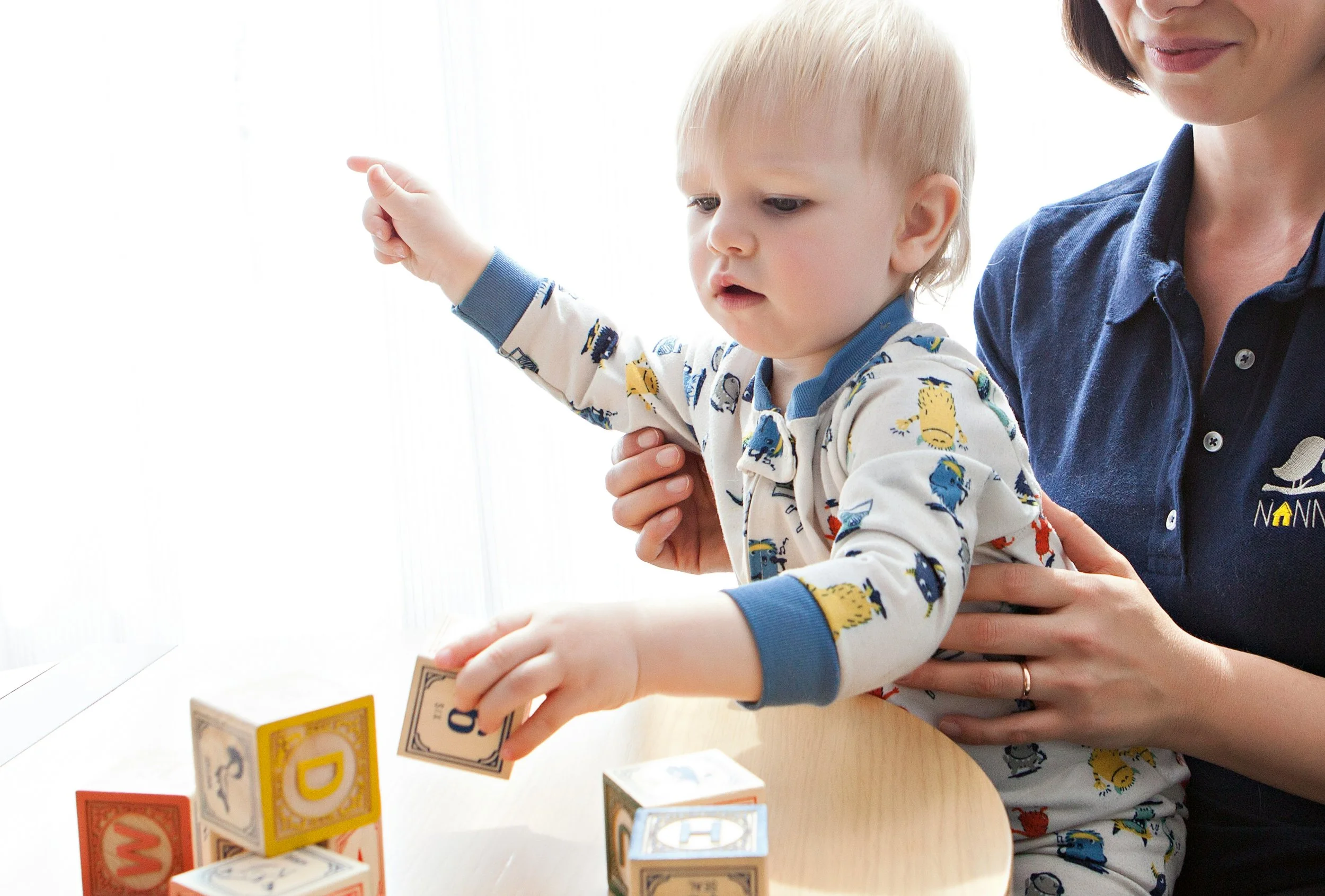 A pediatric occupational therapist working with a toddler, assisting him in standing while playing with blocks.