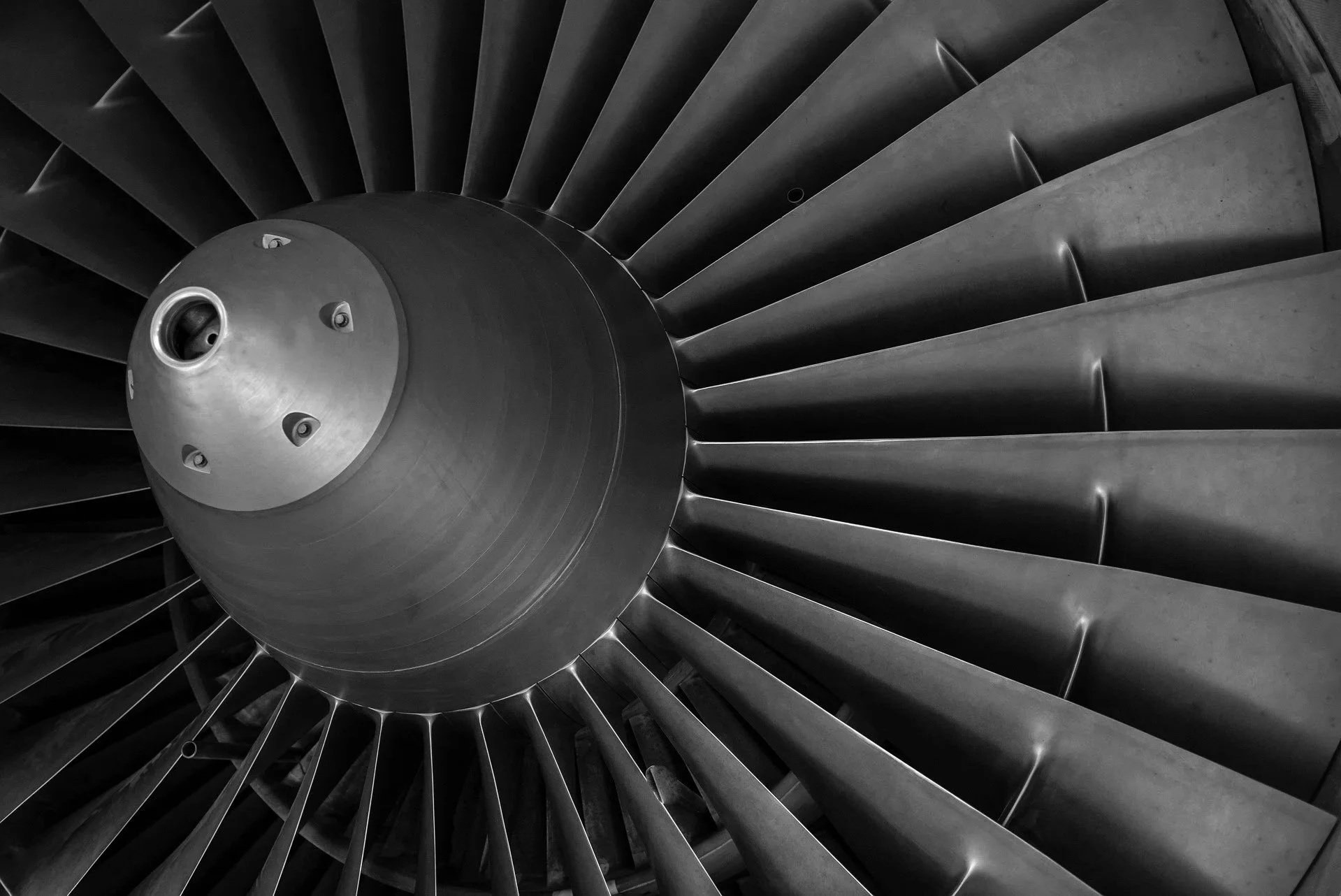 Close-up of a jet engine turbine with visible blades in black and white.