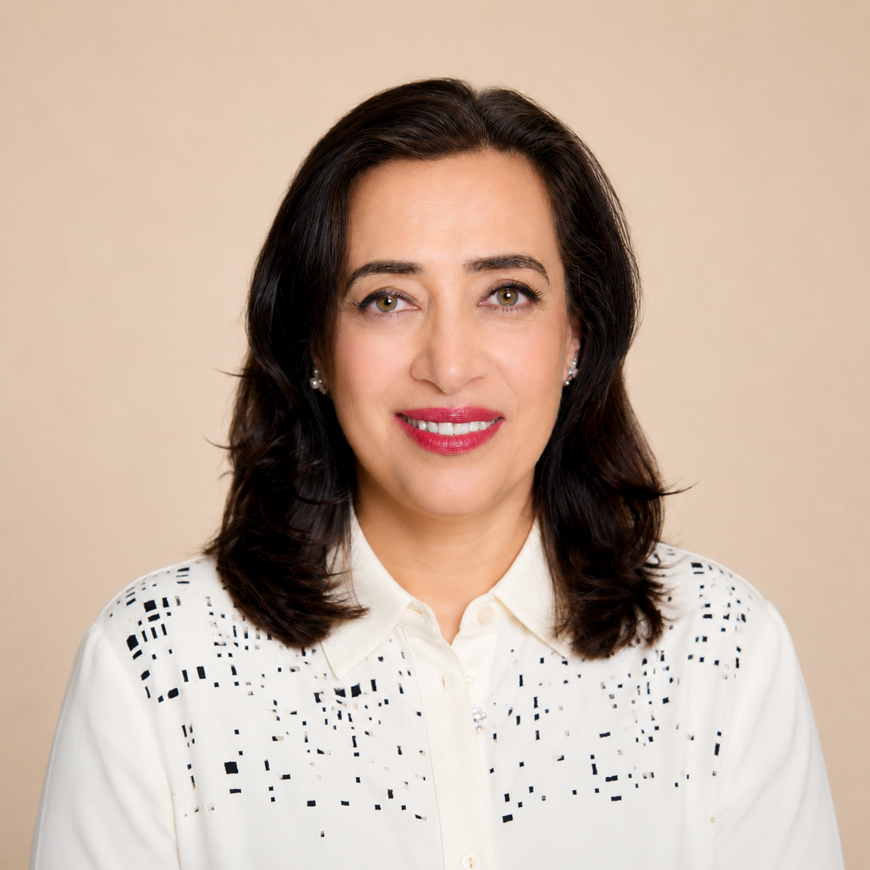A woman with shoulder-length dark brown hair, wearing a white collared shirt with black square patterns, smiling against a beige background.