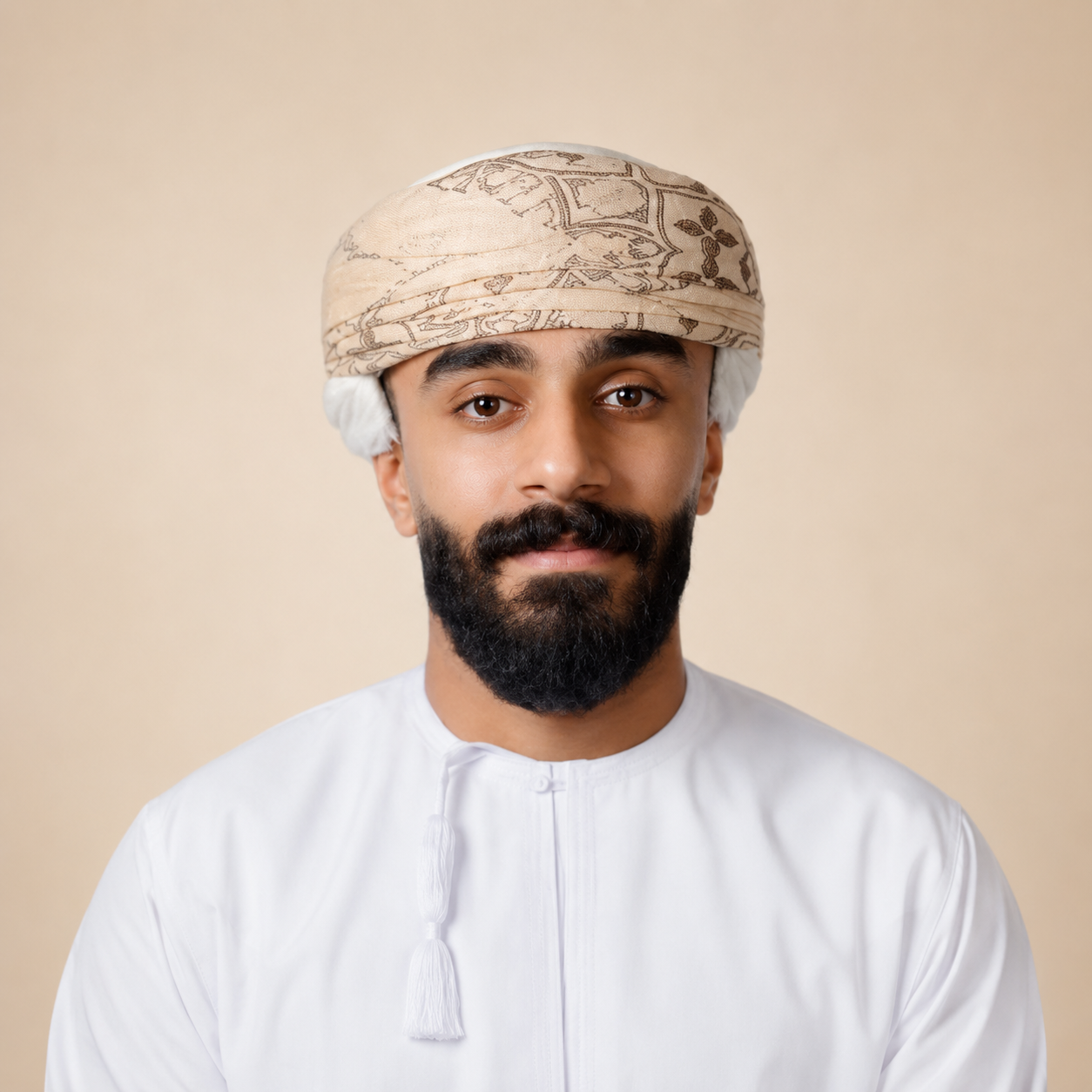 Portrait of a man wearing a traditional head covering and a white thobe, against a beige background.
