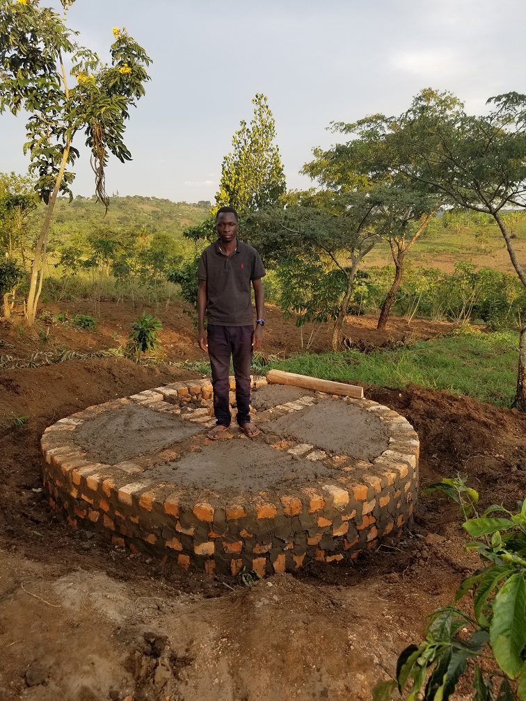 A young man standing on a new brick and cement platform outdoors, surrounded by trees and rural landscape.
