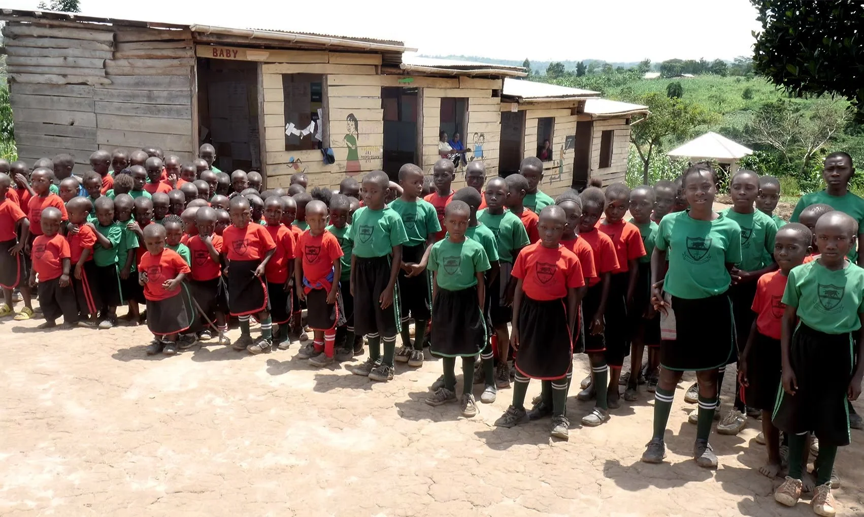 A group of school children in uniform standing outside a small wooden building.