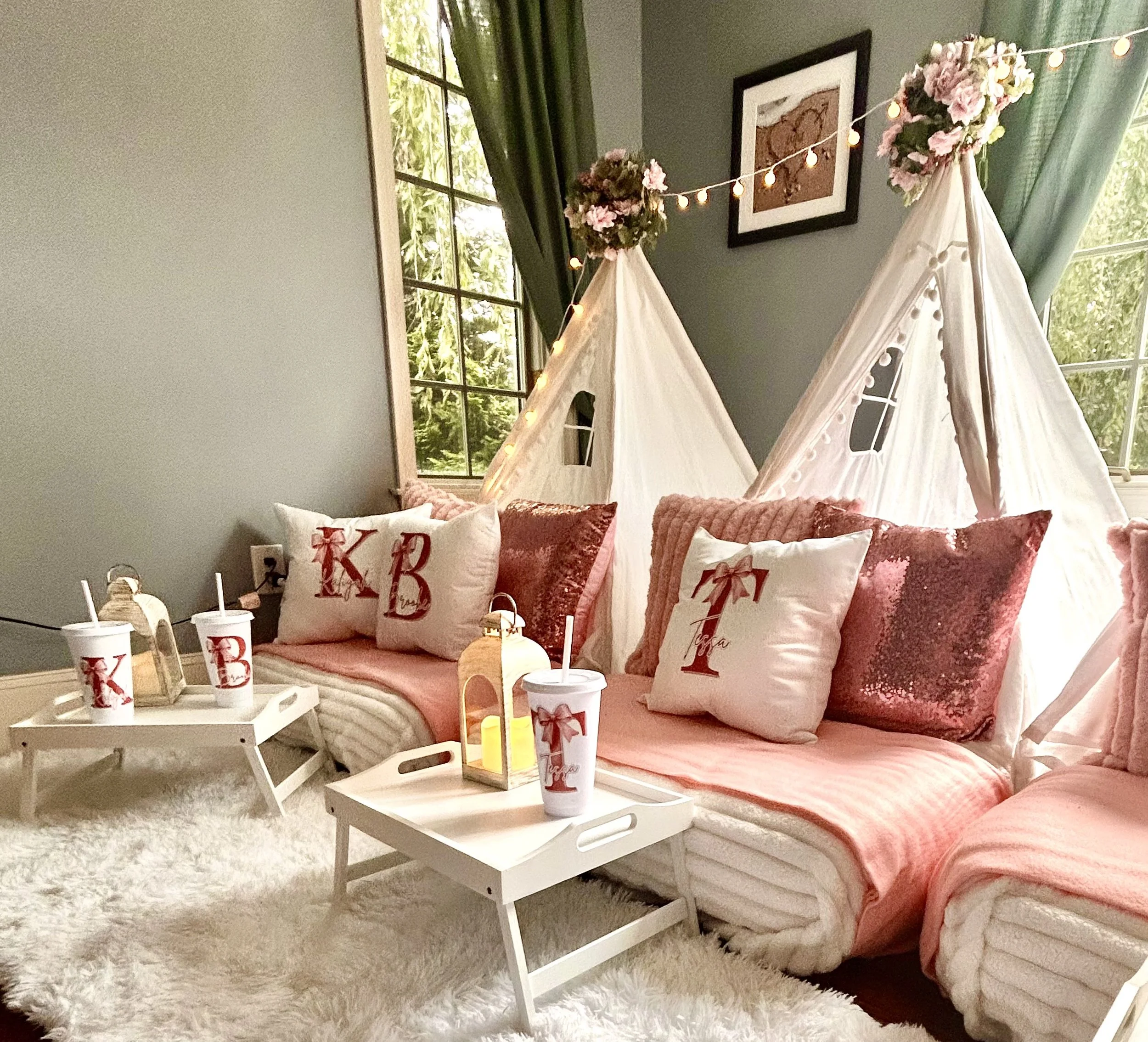 A cozy bedroom decorated for Christmas with white beds and red pillows, a tent with pink flowers and string lights, a white tray with drinks, and a fluffy white rug.