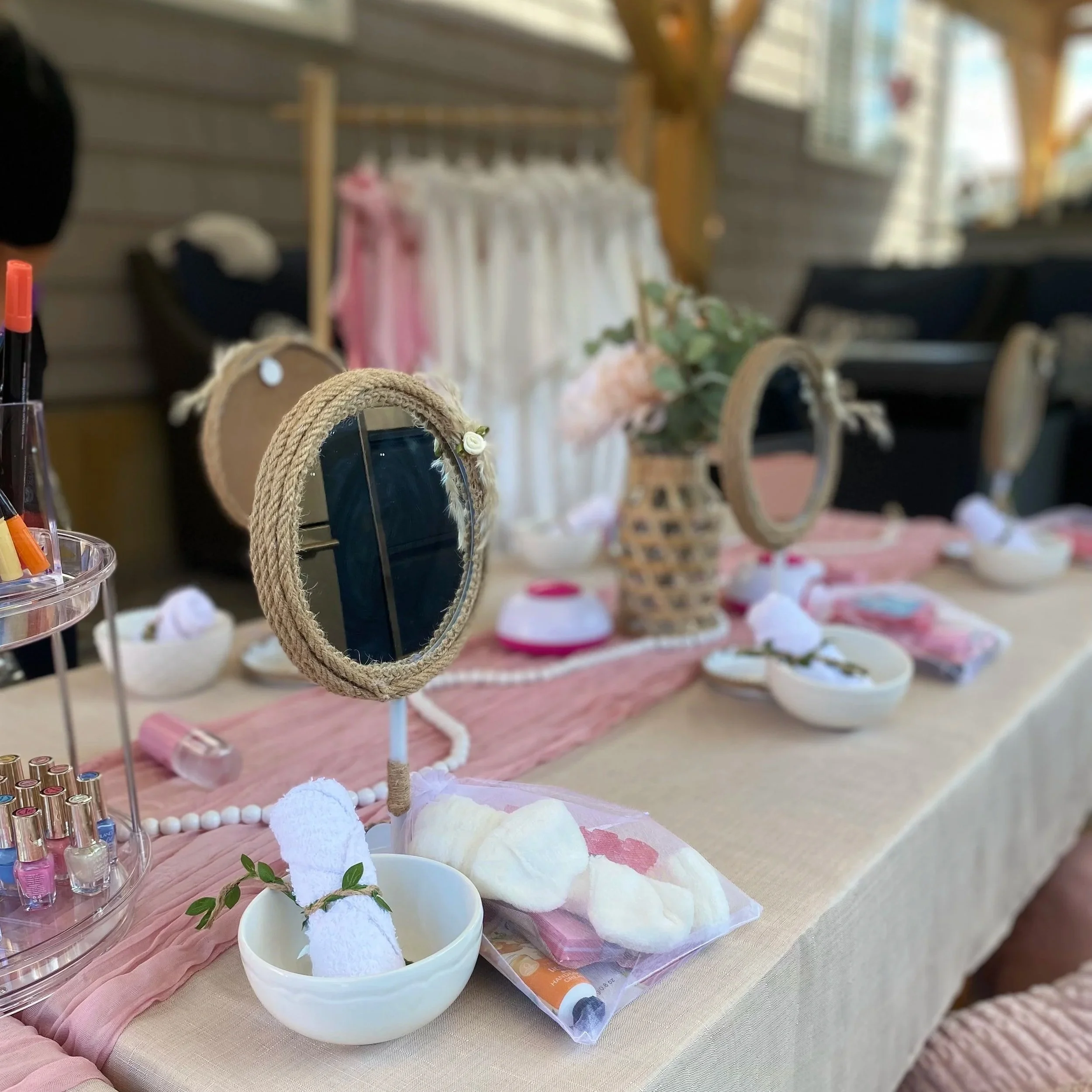 Display of nail polish bottles, small decorative mirrors, and cotton balls on a pink cloth, likely at a beauty or nail salon setup.