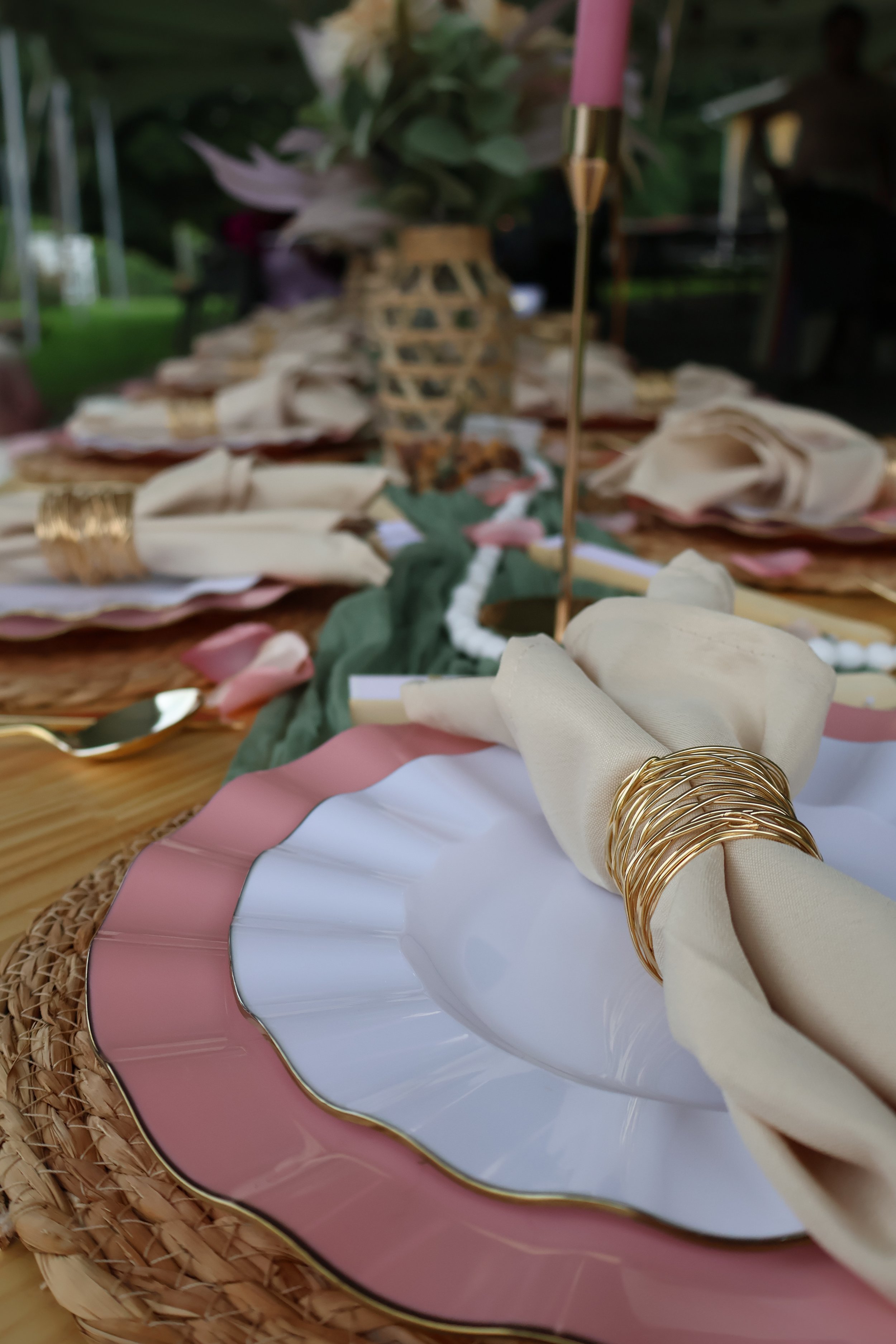 Decorative table setting with pink and white plates, gold accents, and a floral centerpiece with pink and white flowers and green foliage.