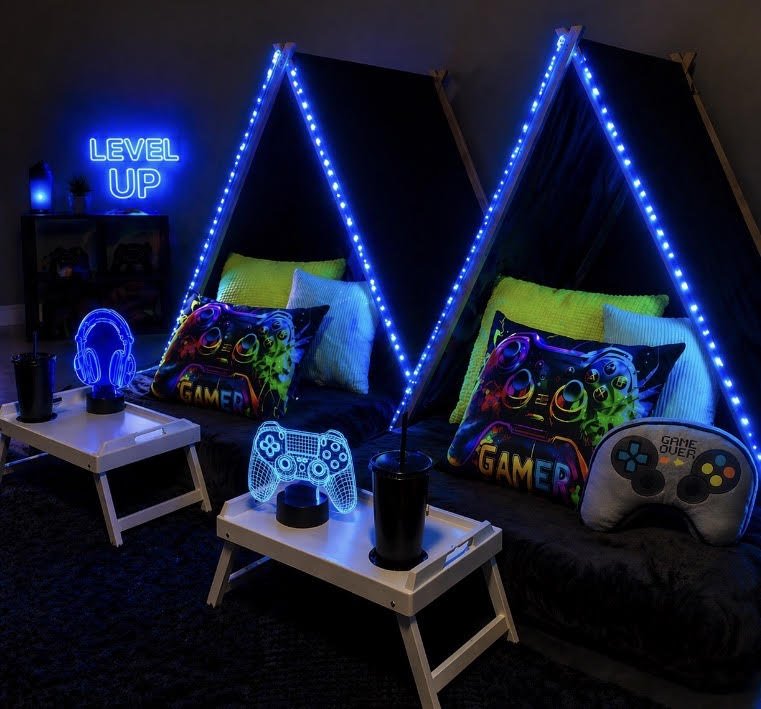 Gamer lounge with two black teepee tents decorated with blue LED strip lights, colorful gaming pillows, LED gaming controller lights, cups with straws, and a neon sign saying 'LEVEL UP' in the background.