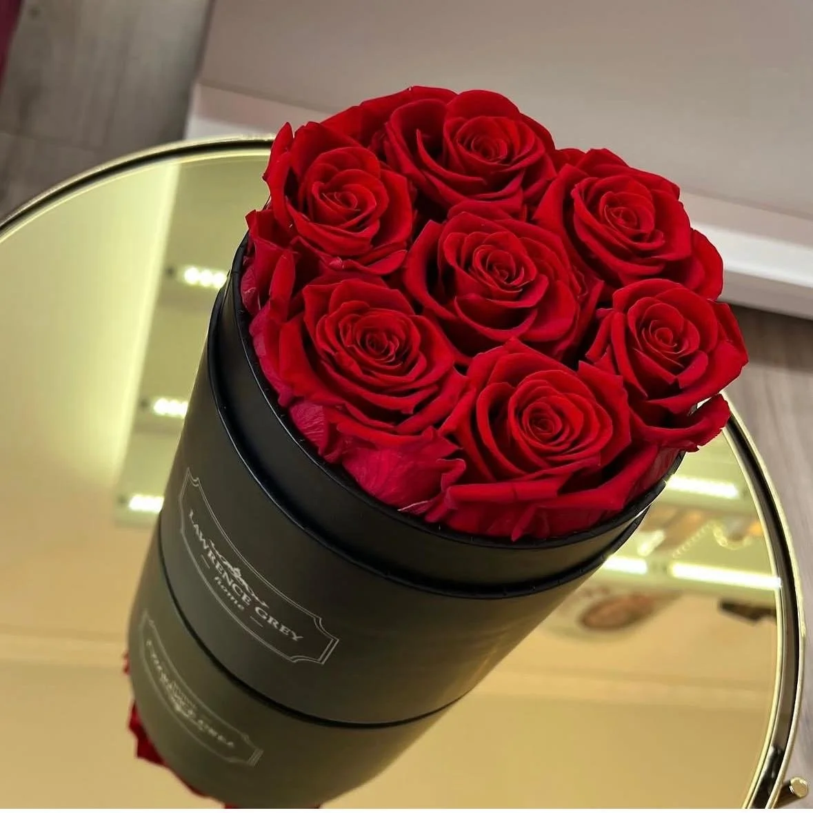 Rote Rosen in einer schwarzen runden Geschenkbox auf einem runden Spiegel.