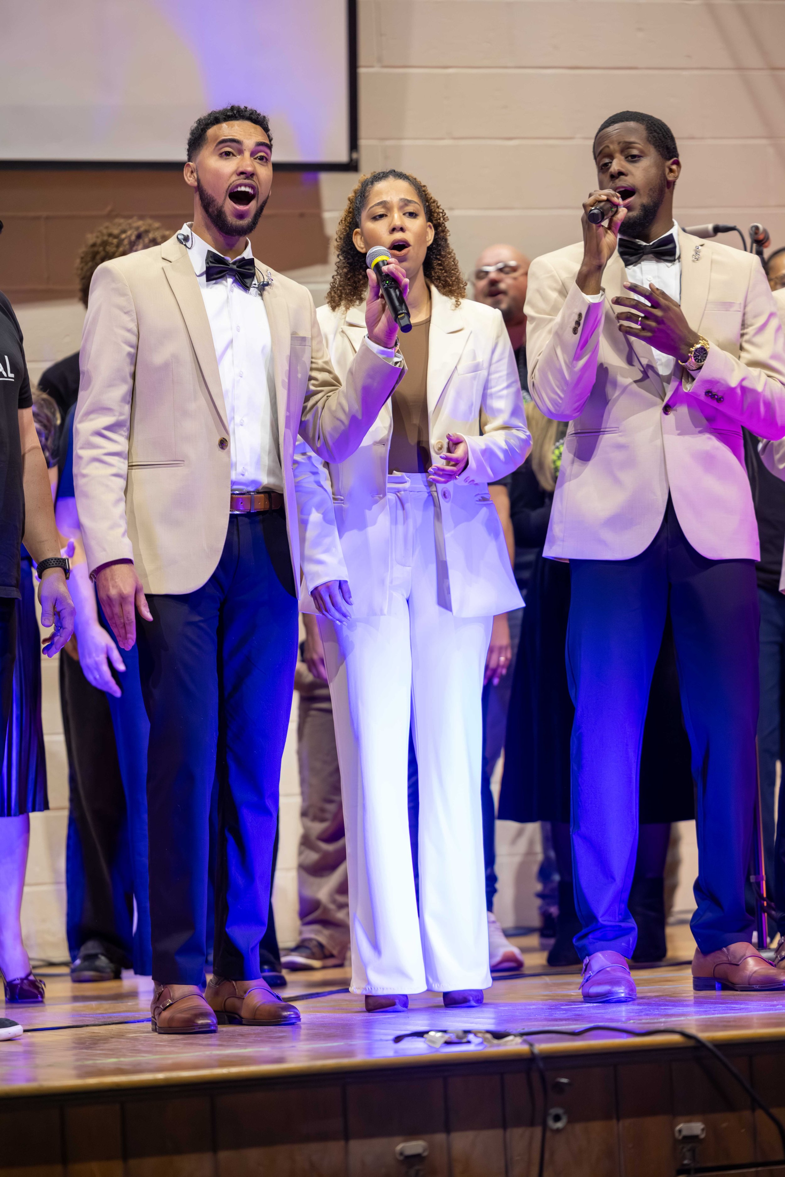 Three singers dressed in formal attire performing on stage, with a male singer on the left, a female in the center, and another male on the right holding microphones. They appear to be singing passionately.
Heralds of freedom 5th annual concert.