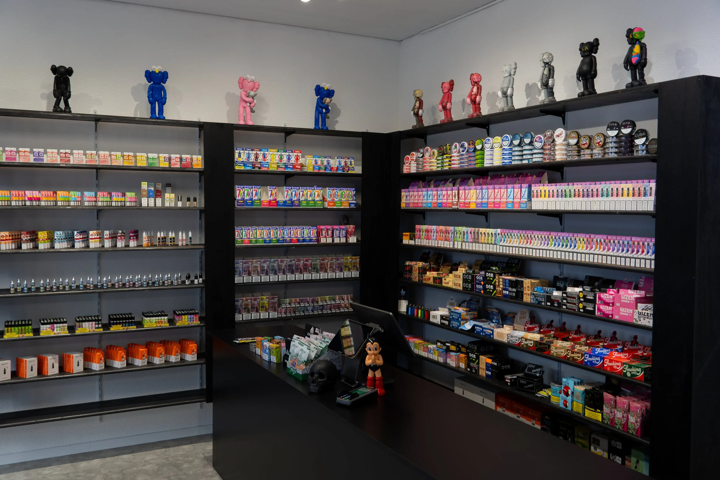 Display of colorful candy and vaping products on black shelves in a store, with decorative figurines on top.