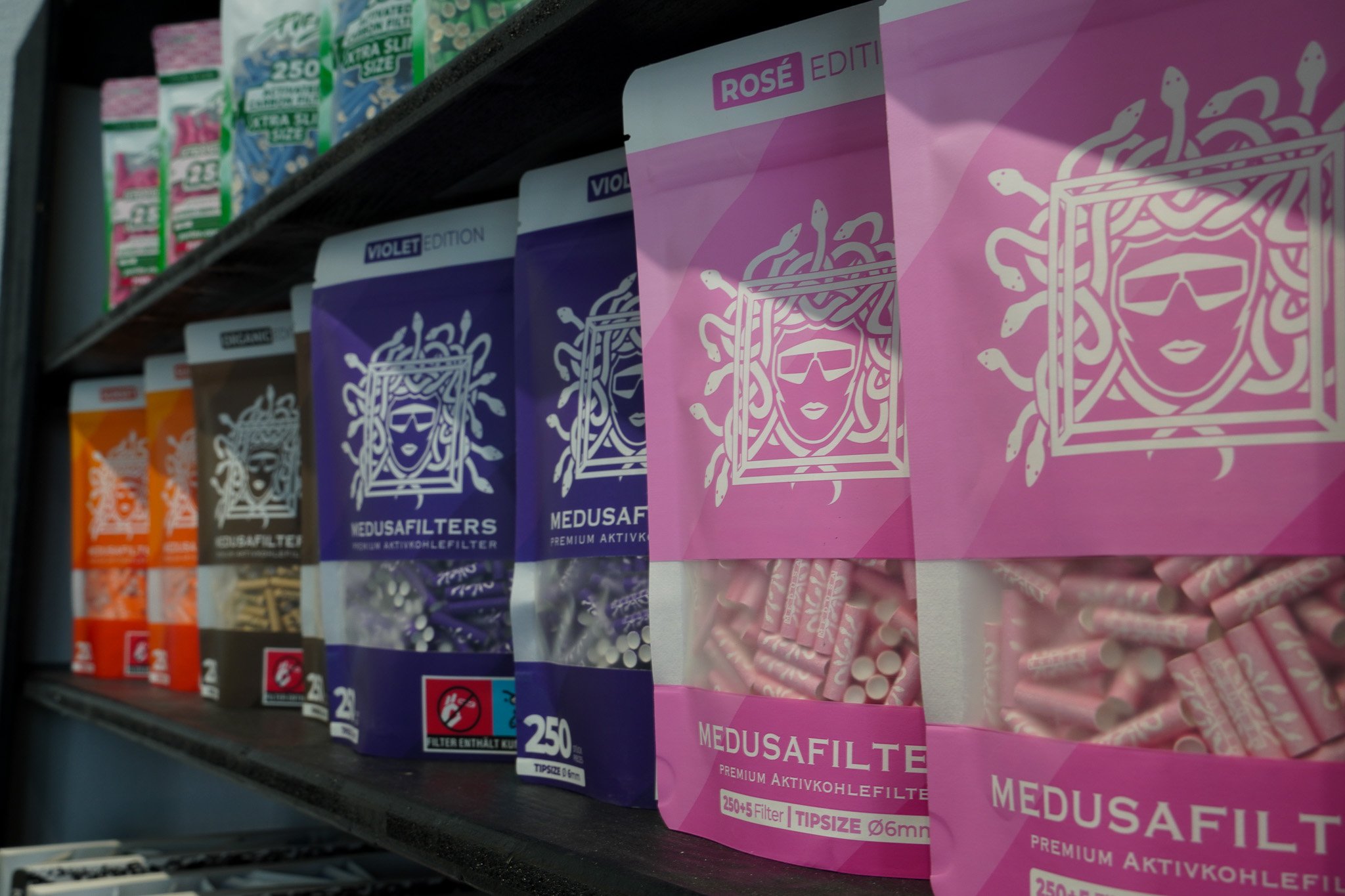 Shelf with boxes of Medusa filter products in various colors, primarily pink, purple, and orange, with graphic designs and branding visible.