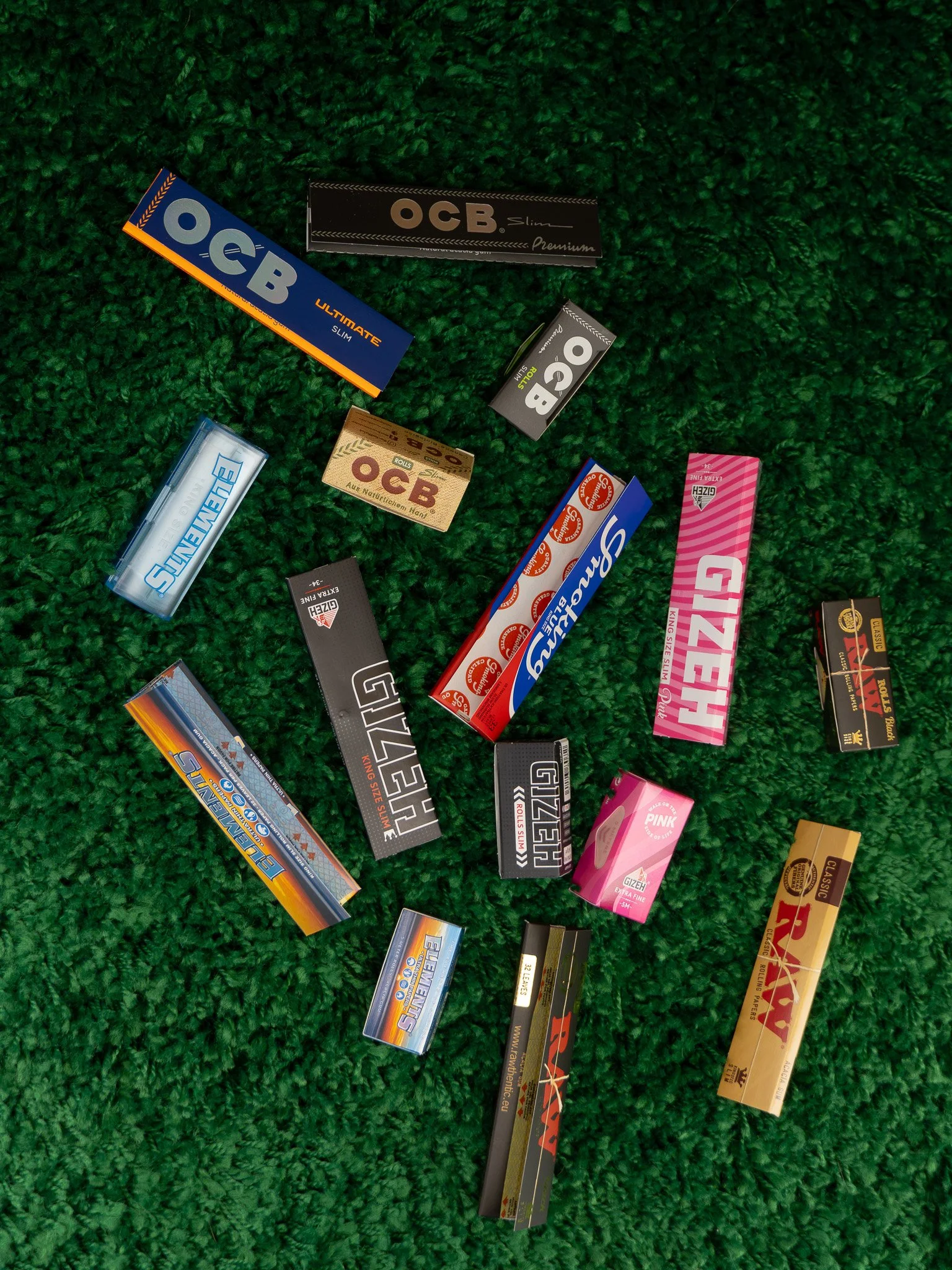 Various cigarette and rolling paper packs scattered on a green textured surface.