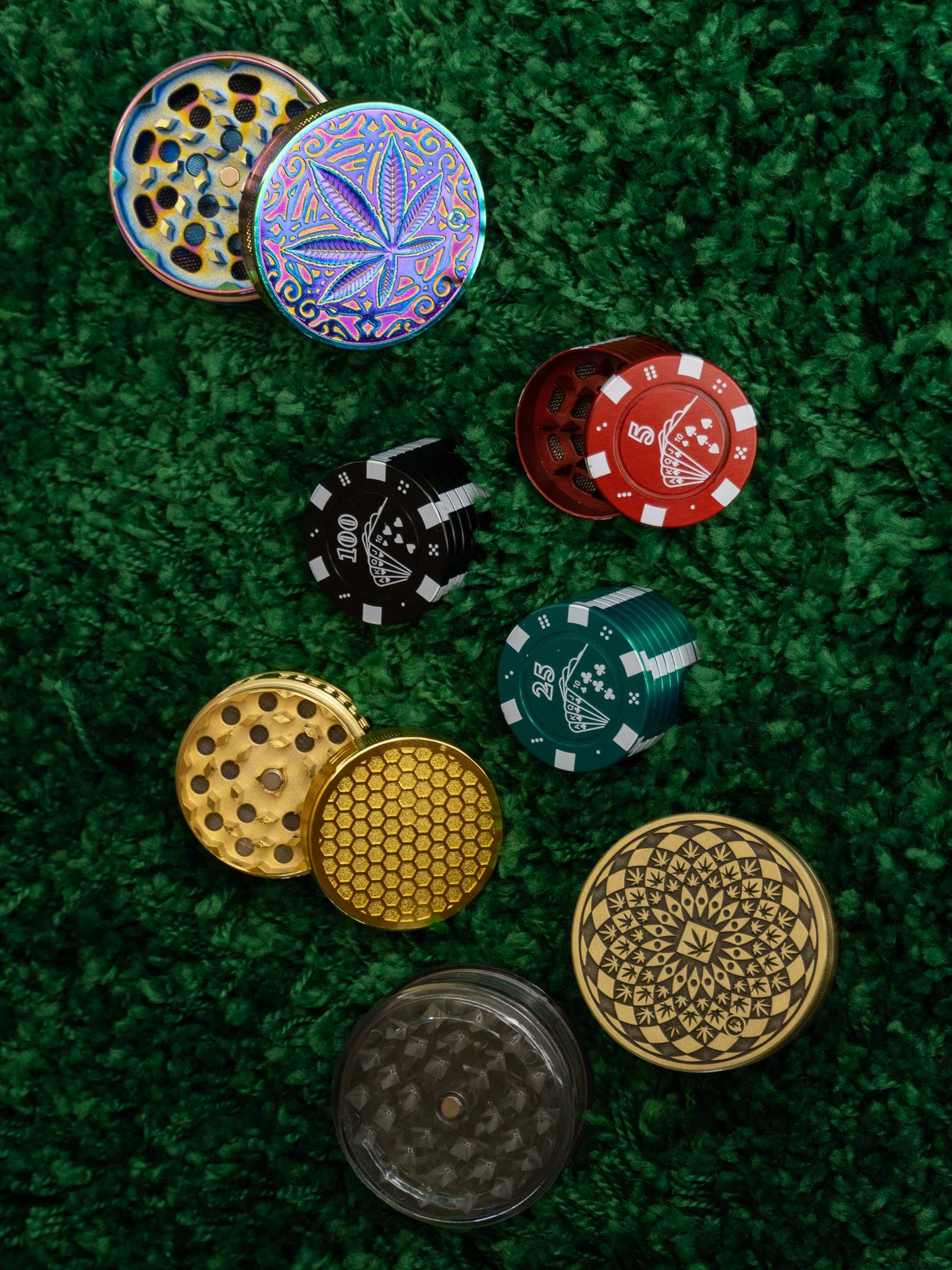 Colored metal and plastic cannabis grinder lids and loose lids on a green textured surface.