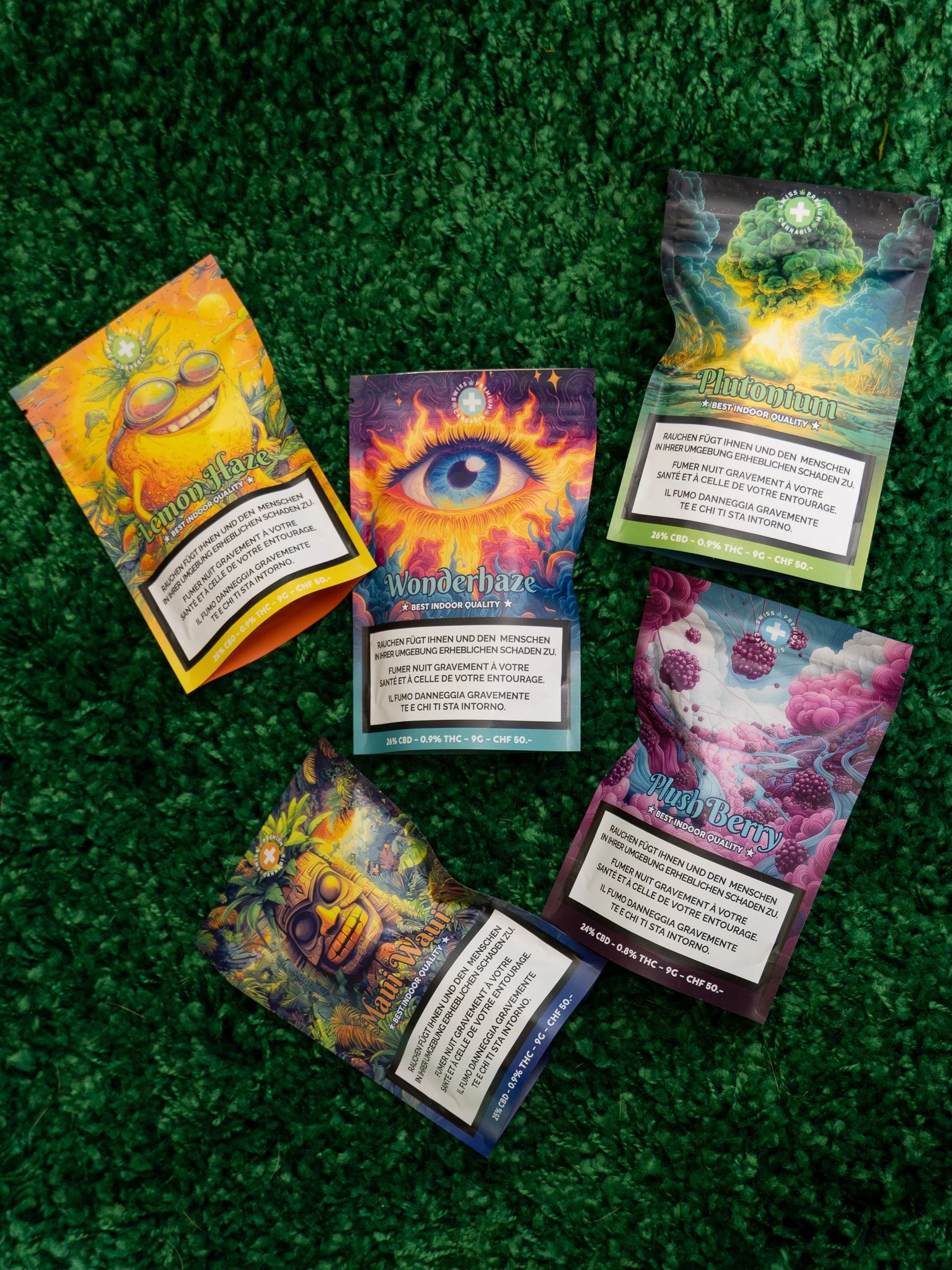 Colorful cannabis product packaging with artistic designs and warning labels, lying on a green textured surface.