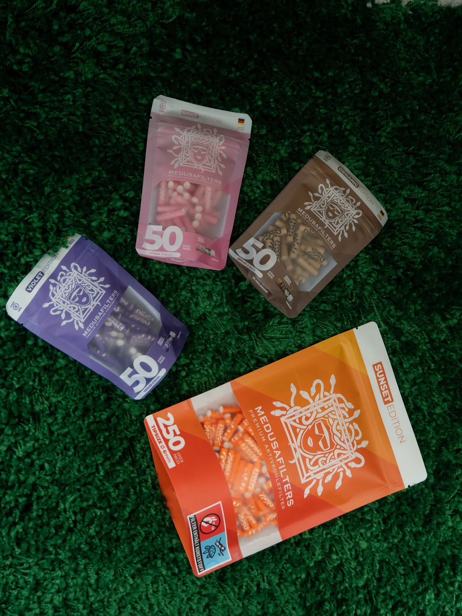 Colorful packages of Medusa filters in purple, pink, brown, and orange, scattered on a green textured surface.