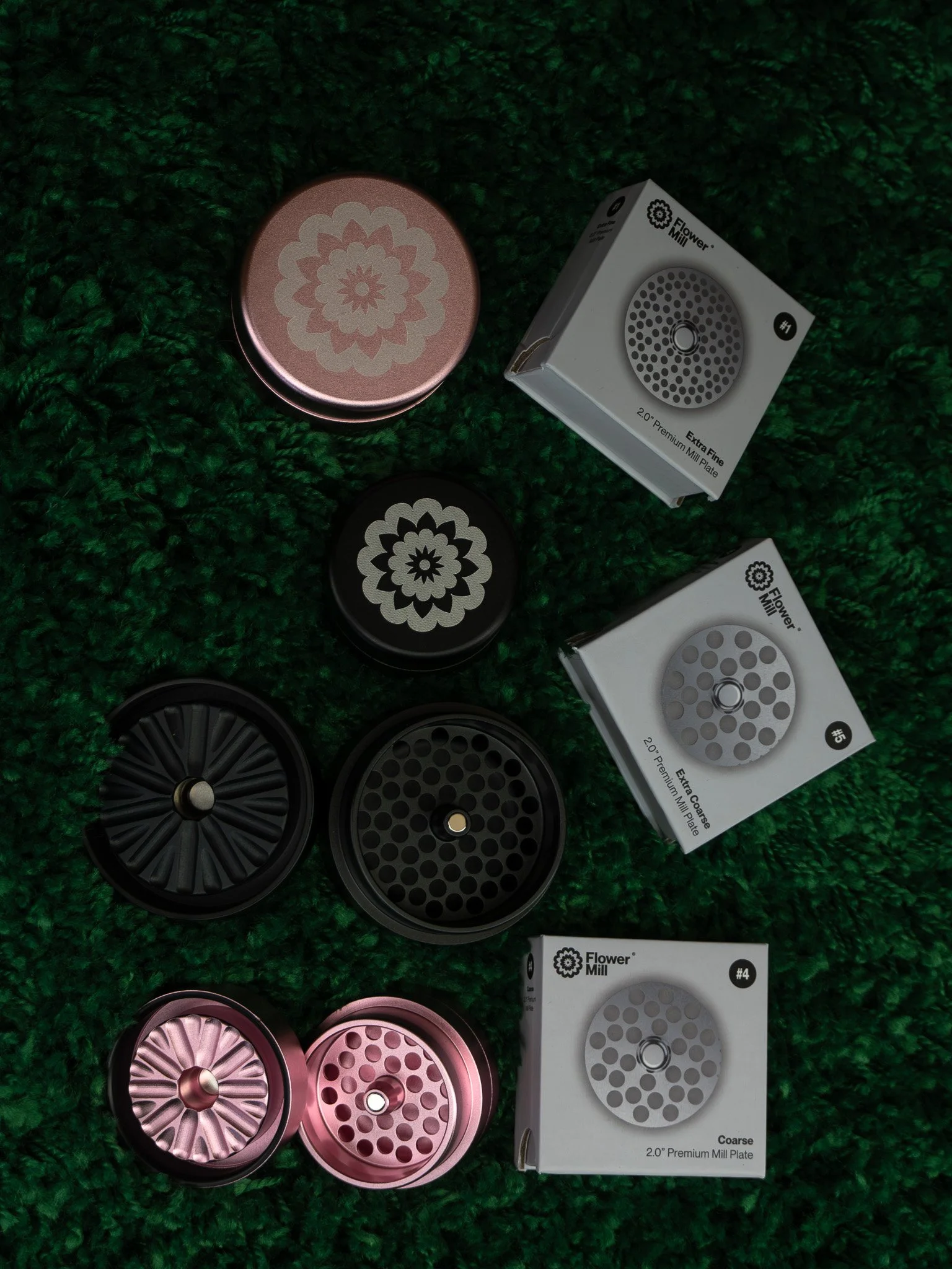 Assorted flower mill grinder plates and boxes with various hole sizes on a green textured surface.