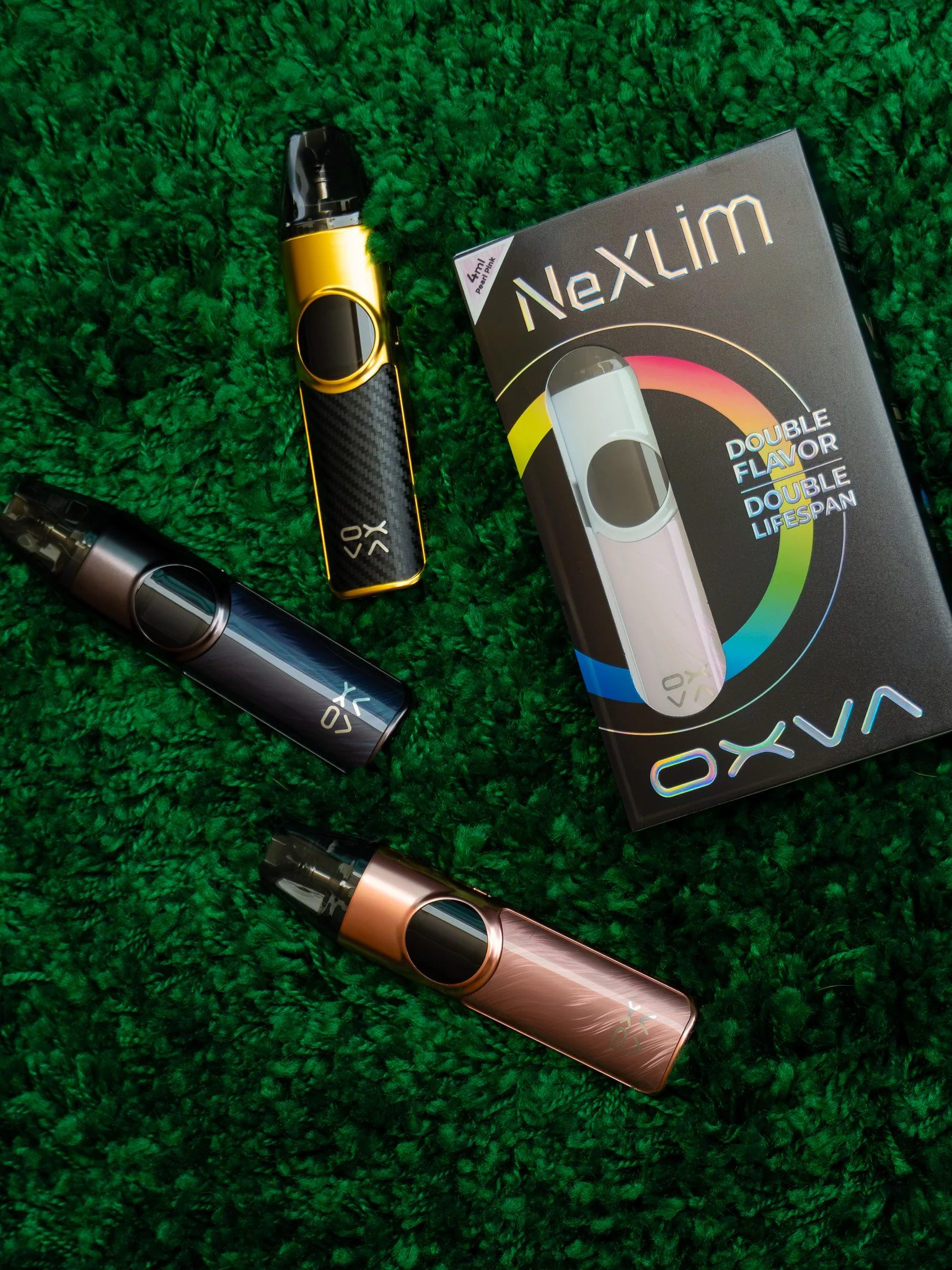 A collection of vape devices and a box of Nexlim nicotine pouches on a green textured surface.