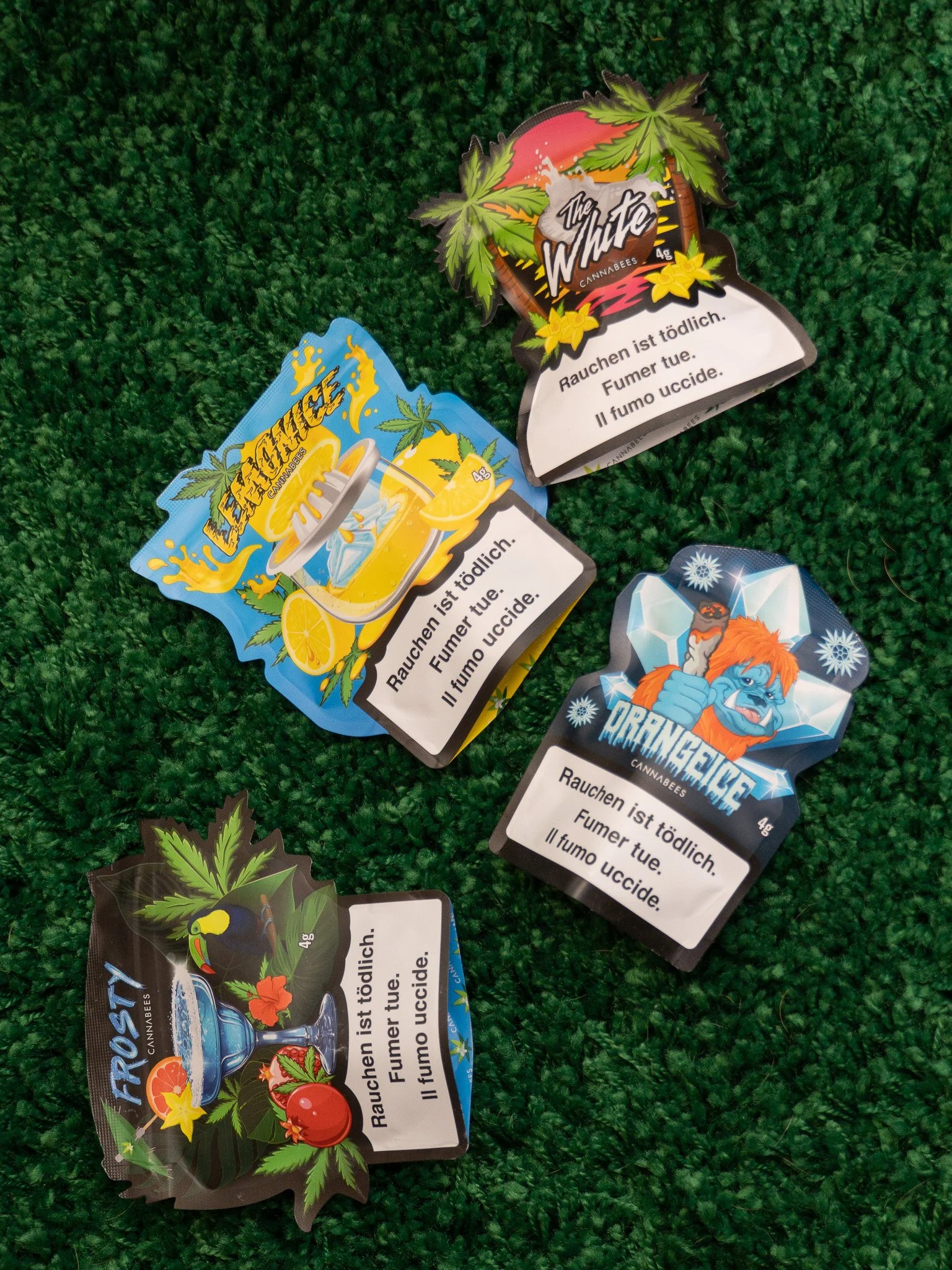 Various colorful cannabis-themed stickers on a green textured surface, with warnings in multiple languages about the health risks of smoking cannabis.