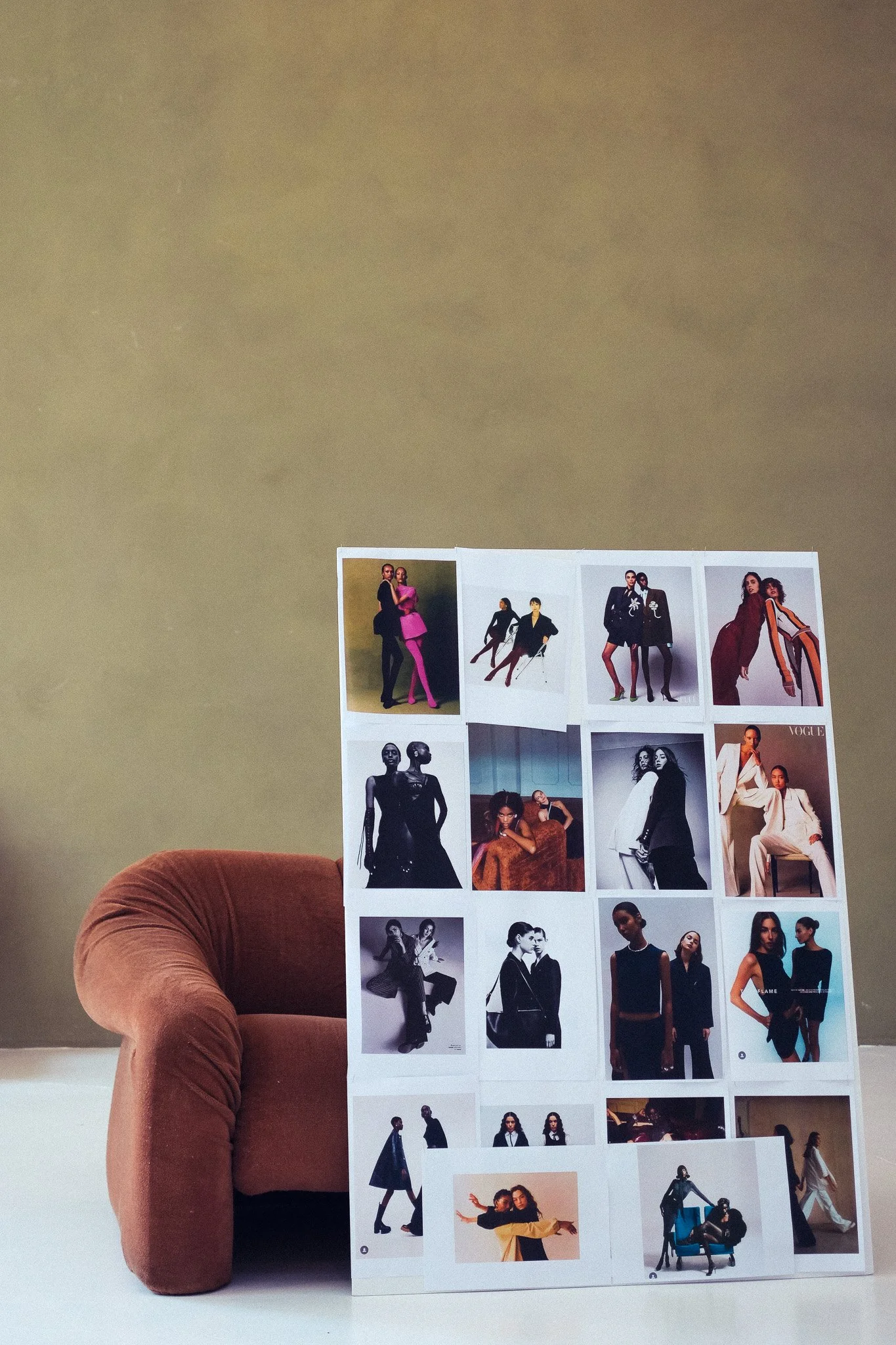 A person's arm and hand holding a sheet of fashion magazine photos against a plain wall background. The photos feature women in various fashion poses and outfits.