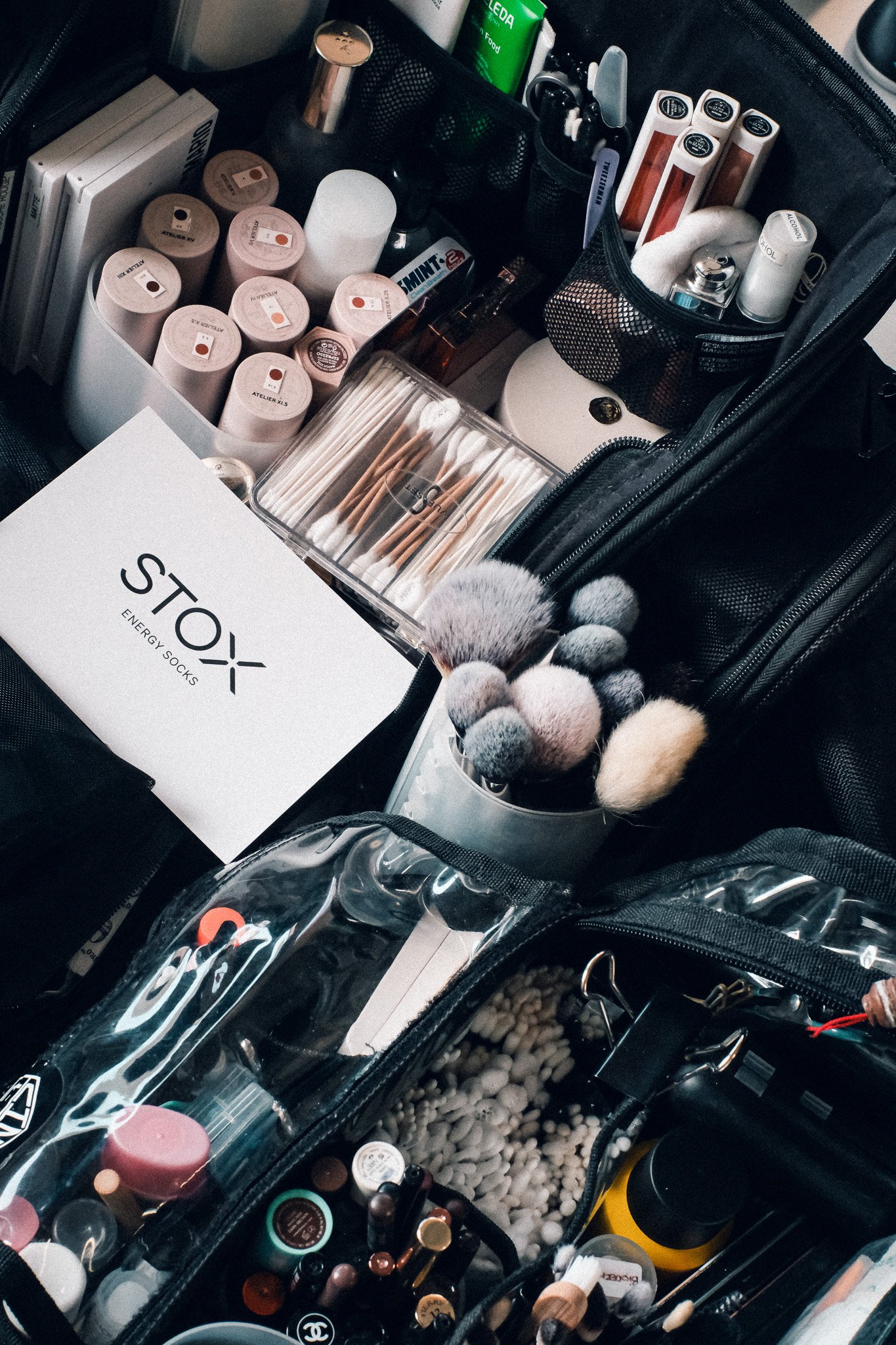 A makeup bag containing various cosmetics, including lipsticks, brushes, cotton swabs, and skincare products organized in compartments.