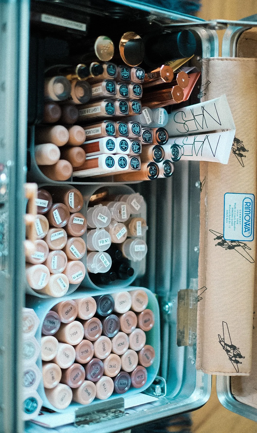 A collection of makeup foundation and concealer tubes organized in a box, with labels indicating shades and types.