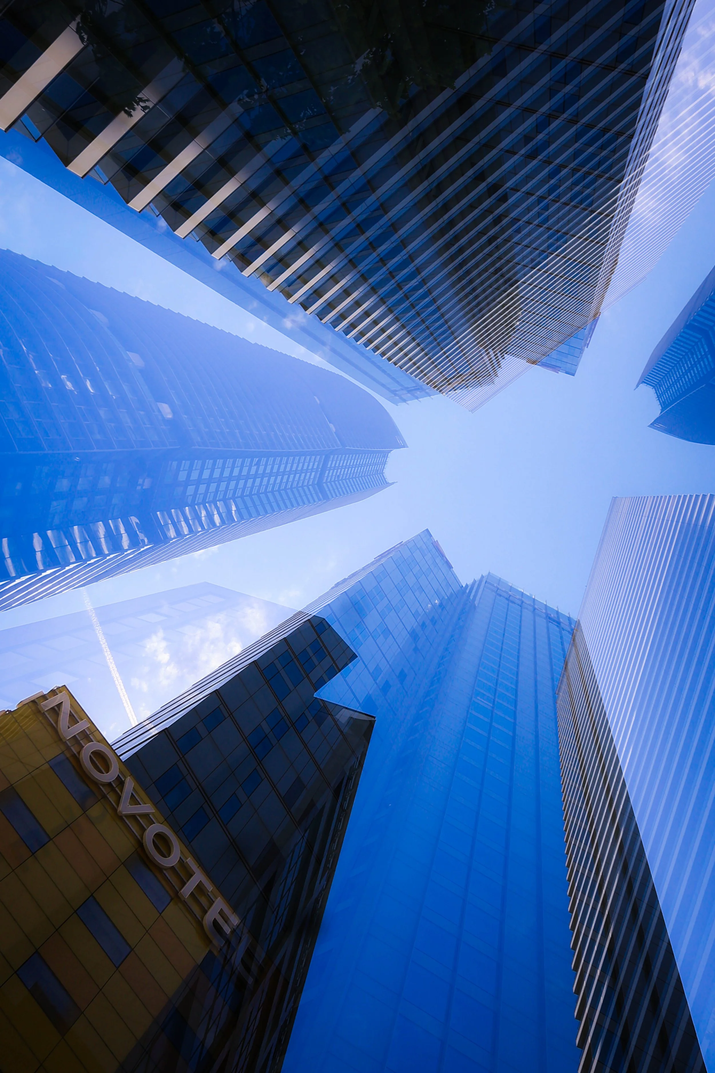 Looking up at tall modern skyscrapers with glass facades reflecting the blue sky and clouds.