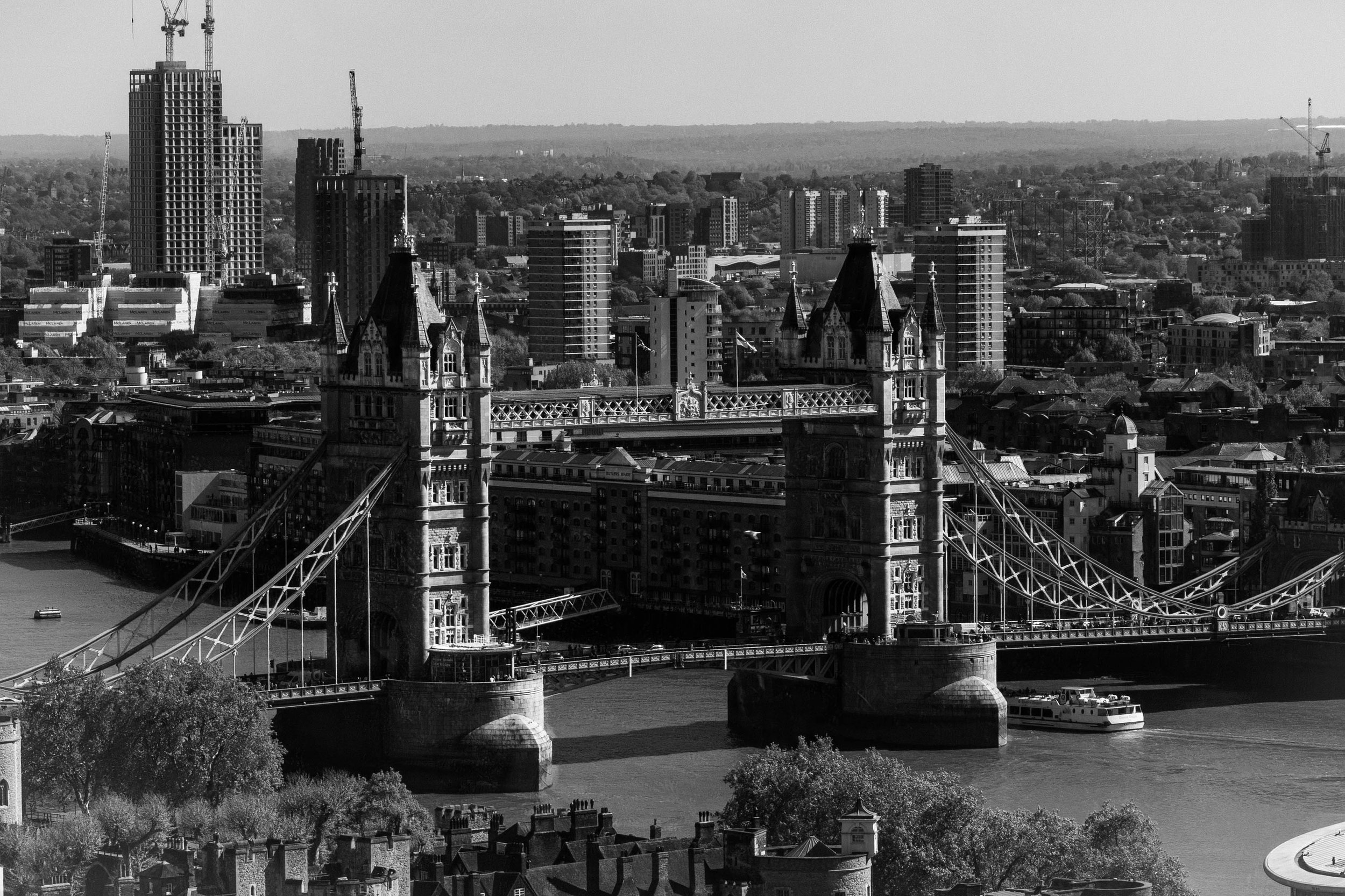 Black and white photo of London Bridge spanning the River Thames with various buildings, including skyscrapers and historic architecture, in the background.