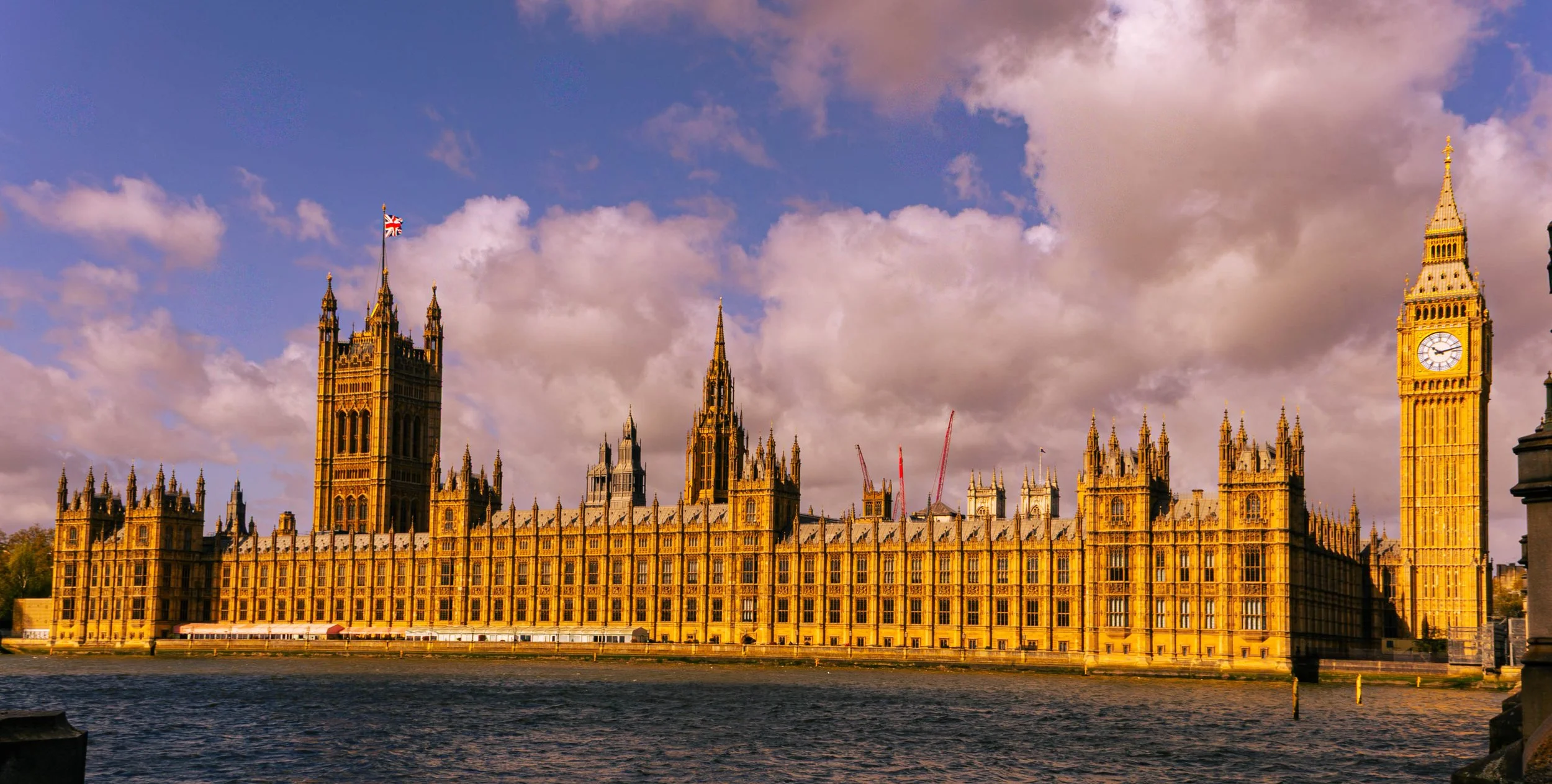 View of the Houses of Parliament and Big Ben clock tower in London, England, during the daytime with a partly cloudy sky.