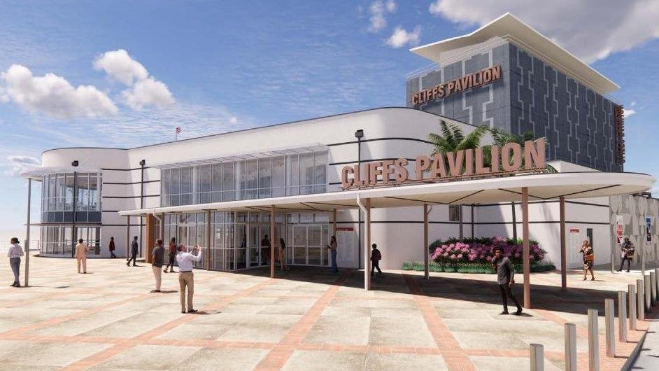 A modern building labeled "Cliff's Pavilion" with a large entrance, palm trees, and a flower bed in front, with people walking around outside on a bright day.