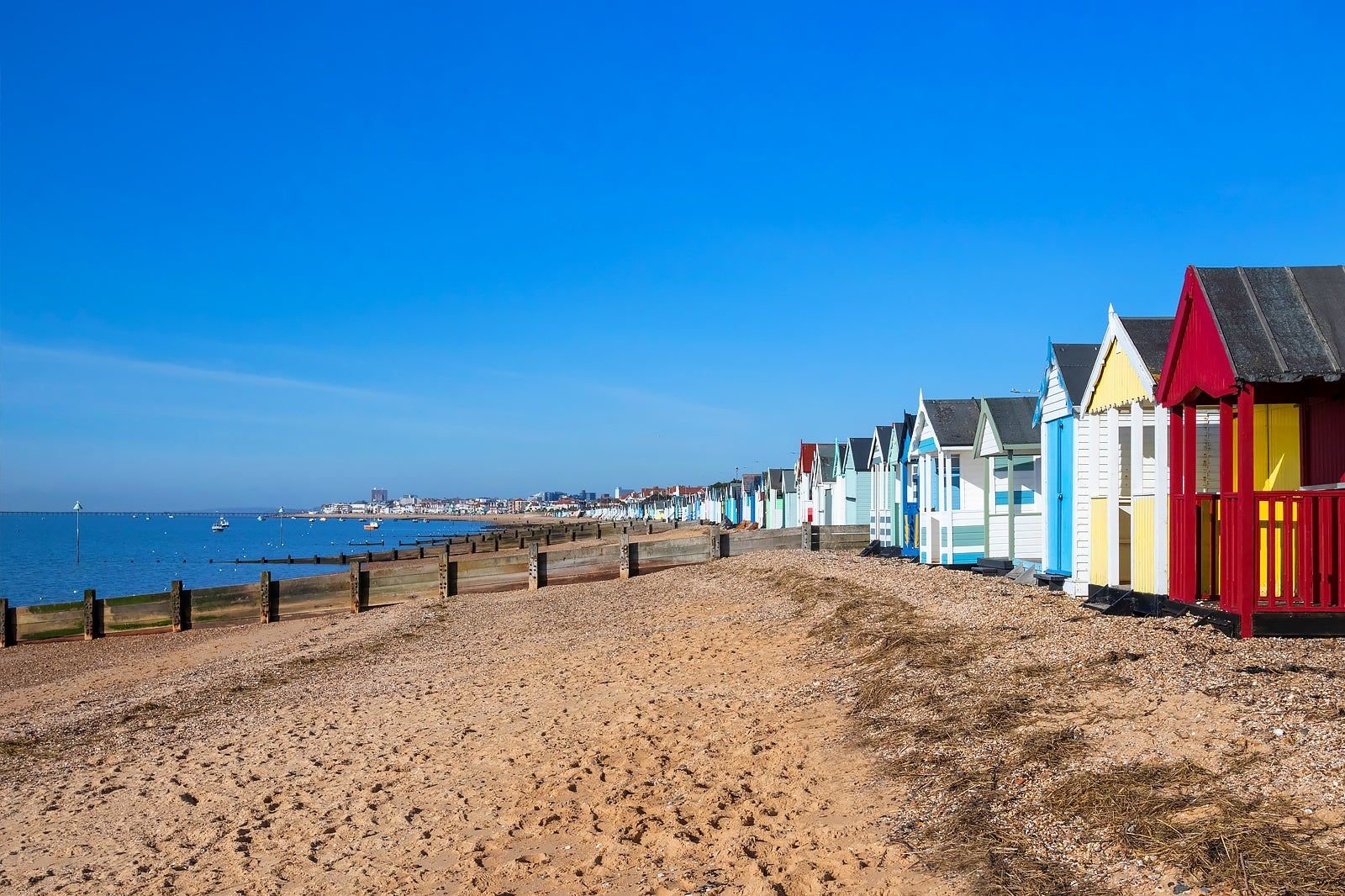 Row of colorful beach huts along the sandy shoreline with calm blue sea and a clear blue sky in the background.