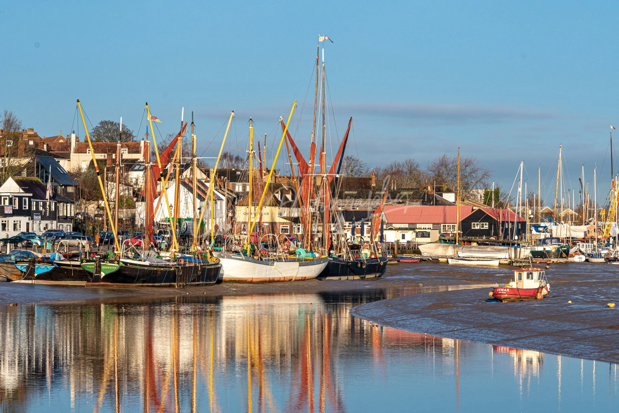 Boats docked along a waterfront with houses and trees in the background on a clear day.
