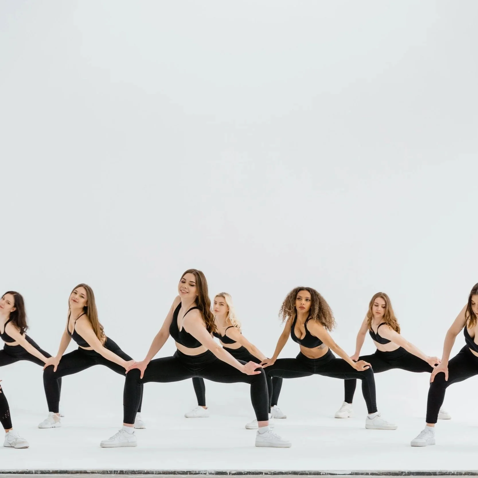 Group of women in black athletic wear stretching in a studio.