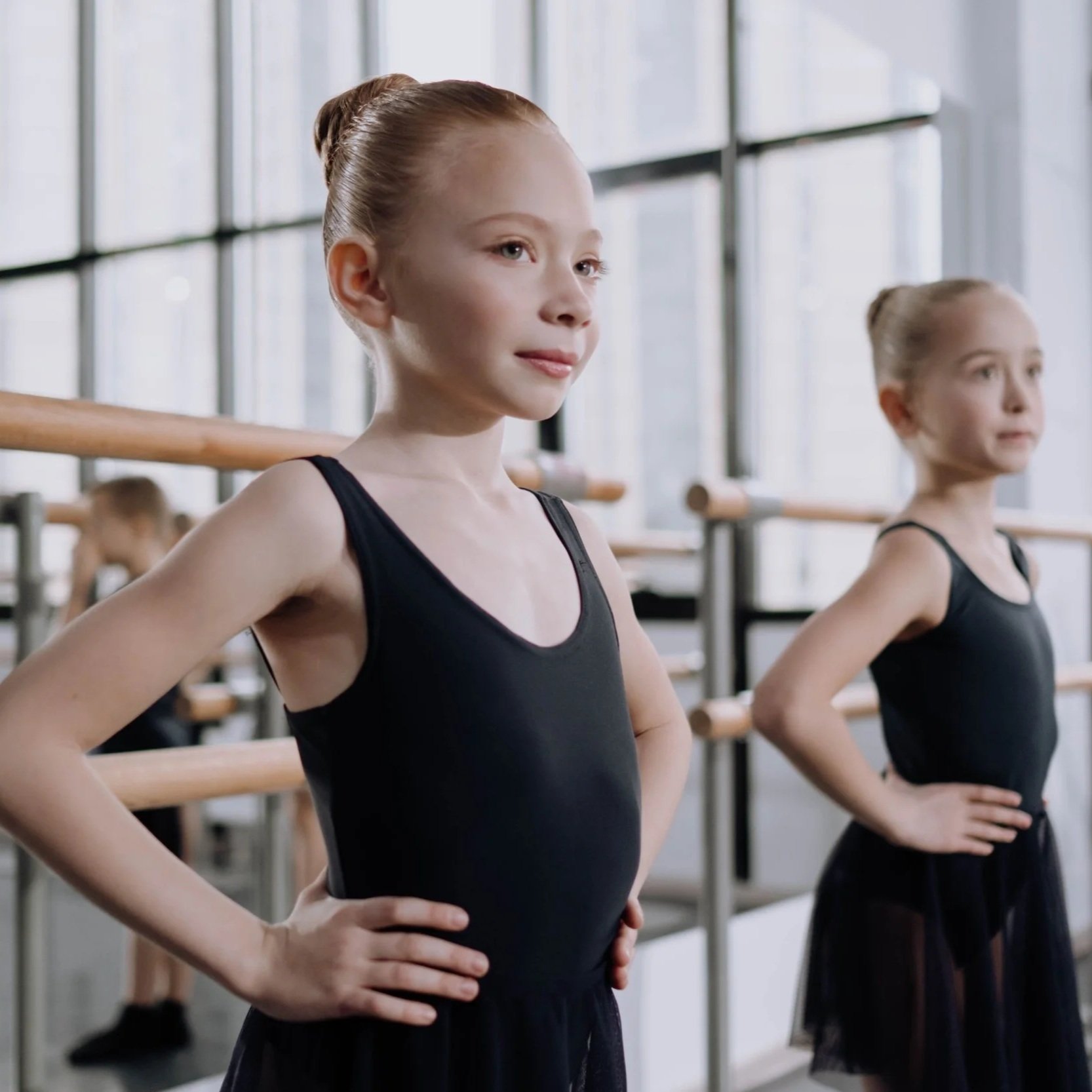 Young ballet dancers in black leotards standing at the barre in a dance studio, ready for practice.