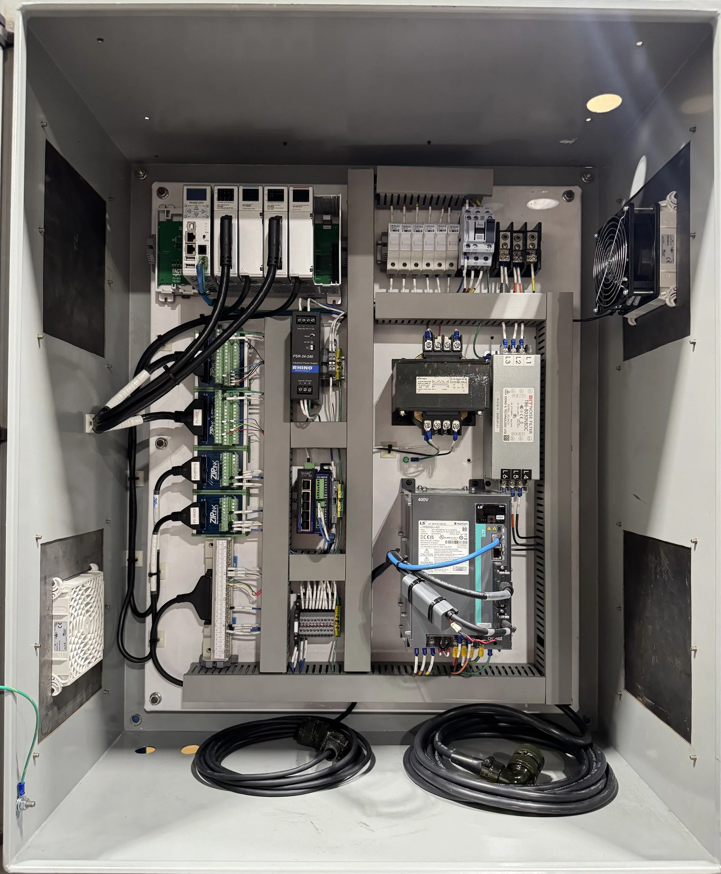 Electrical control panel with various electronic components, wiring, and cooling fan inside a gray metal box.
