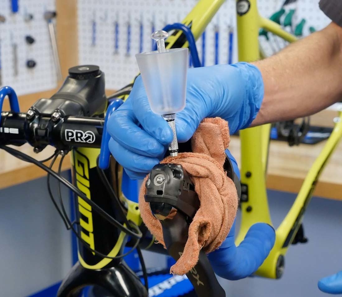 A person wearing blue gloves cleaning a bicycle handlebar with a spray bottle and a cloth in a workshop.
