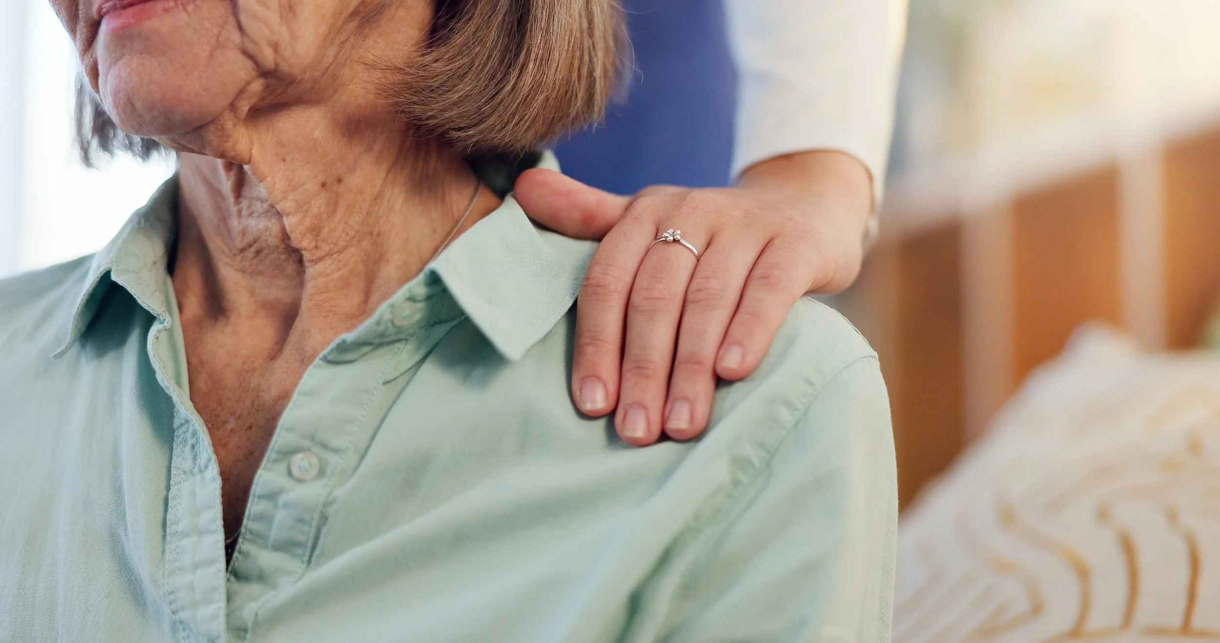 A carer with a reassuring hand on an older woman's shoulder