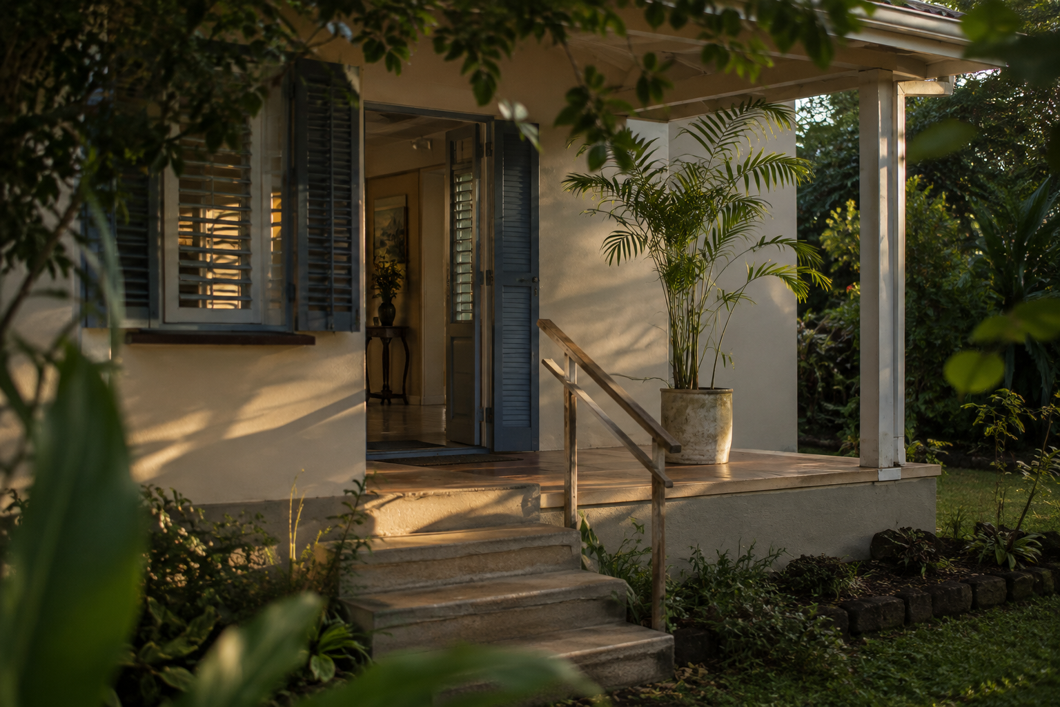 Concrete steps up to the verandah of a Mauritian home, with louvred shutters and tiled floors inside