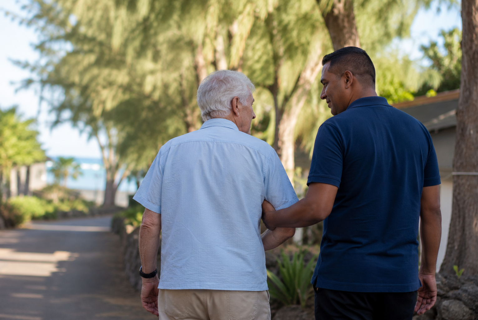 A live-in carer walking with an elderly man along a quiet lane in northern Mauritius