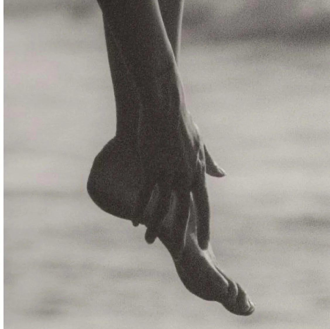Close-up of a ballet dancer's foot en pointe, wearing a ballet shoe, with the other foot raised behind in a dance pose.